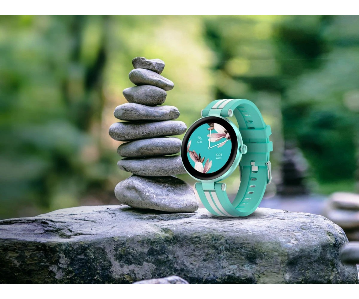 Miętowy smartwatch stoi obok stosu zrównoważonych kamieni na dużej skale na rozmytym zielonym tle.