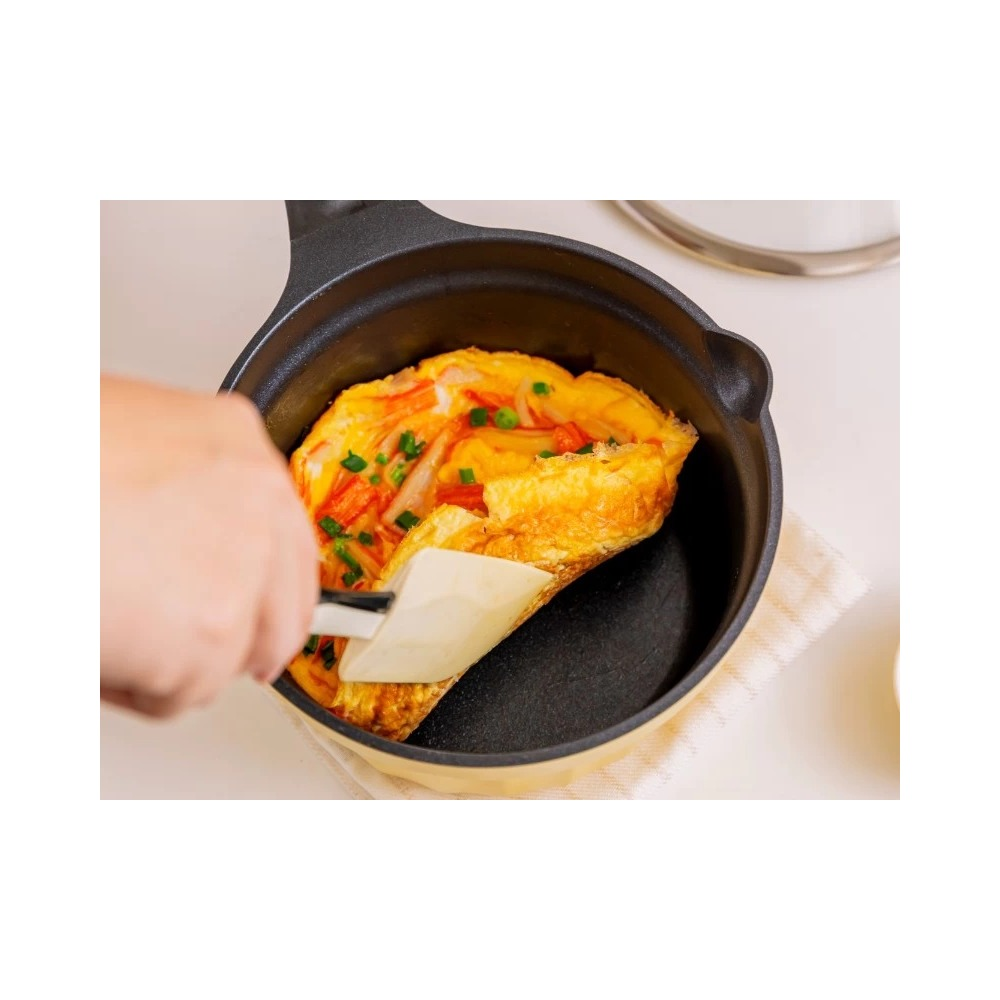 Ręka używa łopatki, aby przewrócić omlet warzywny na czarnej patelni.