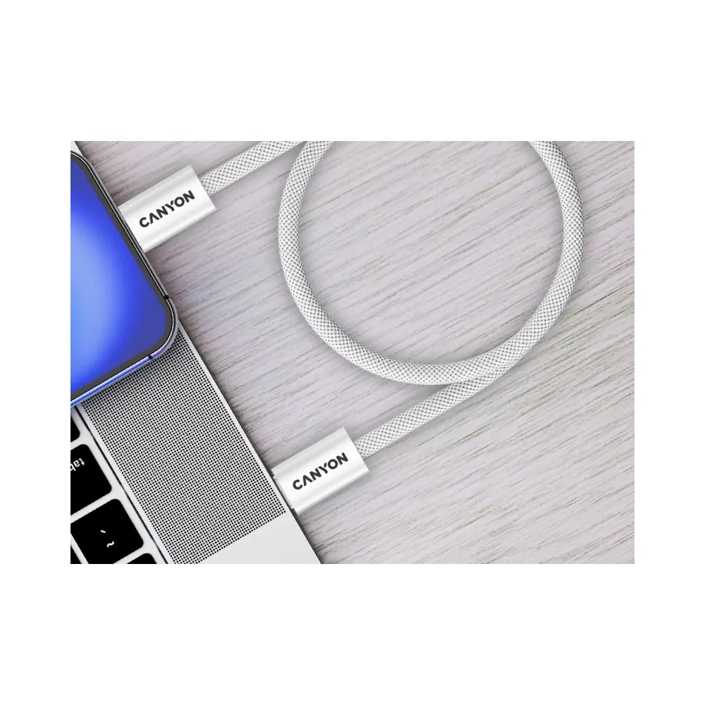 Biały pleciony kabel ładujący Canyon jest podłączony do laptopa na drewnianej powierzchni.