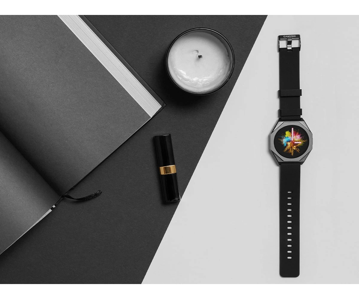 Czarny smartwatch z kolorowym ekranem, świeca, szminka i notes na czarno-białym tle.