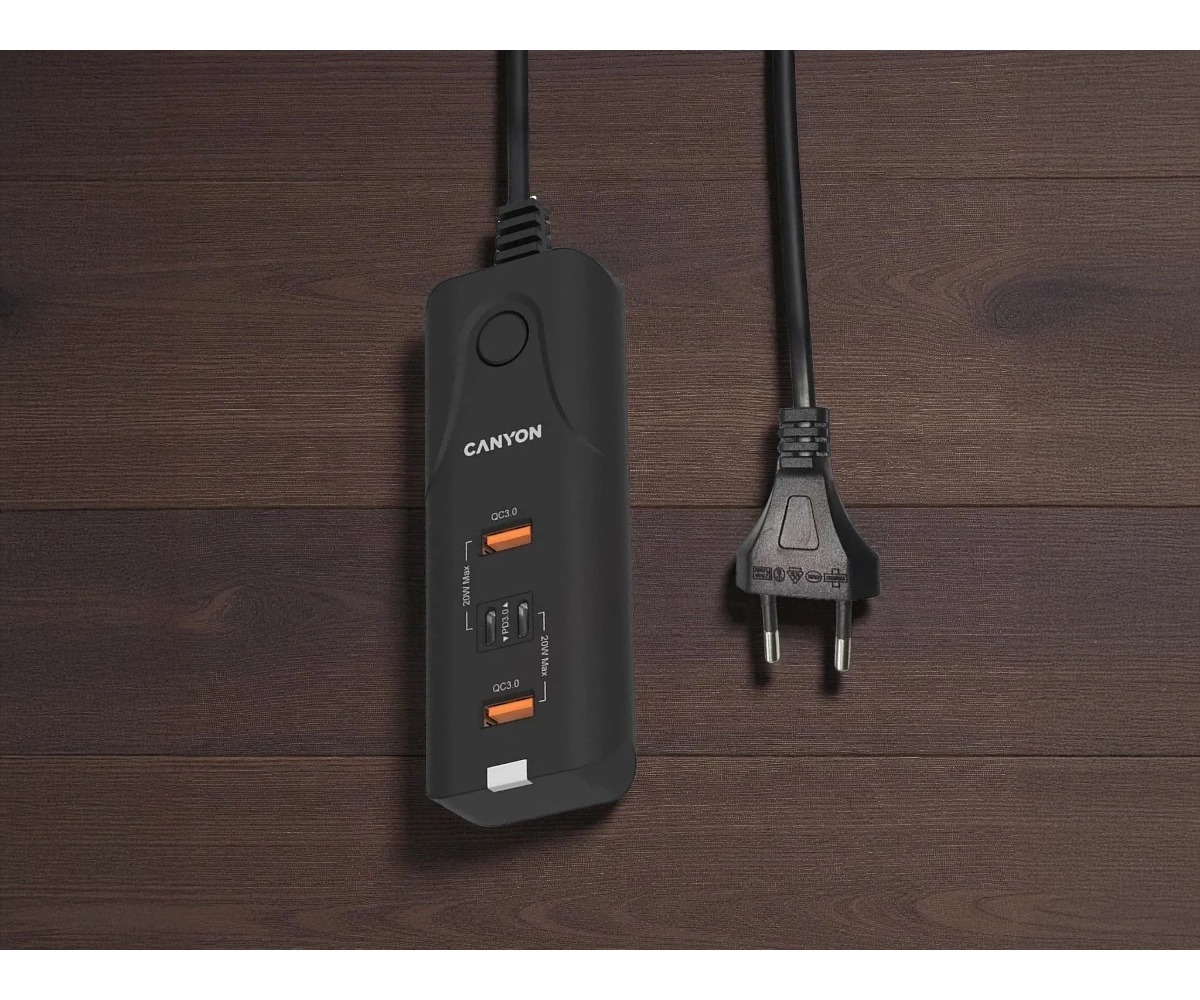 Czarna listwa zasilająca Canyon z portami USB i wtyczką na ciemnym drewnianym tle.