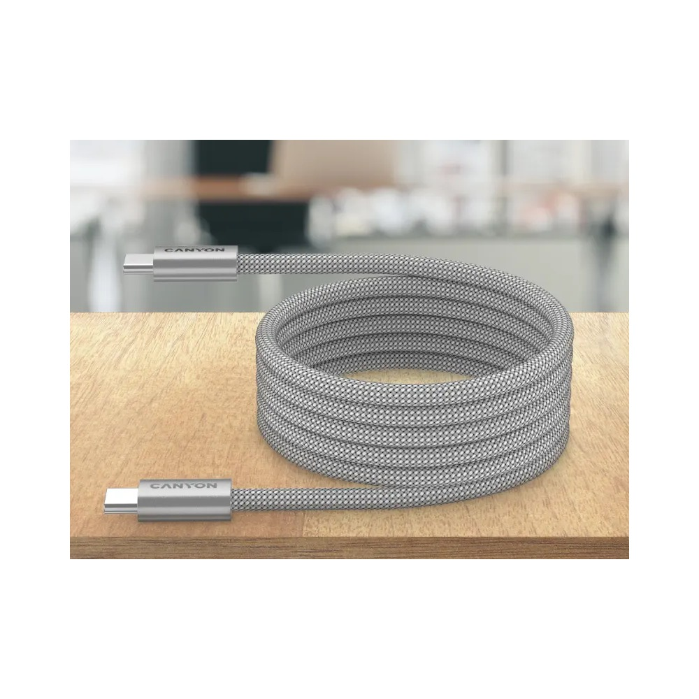 Srebrny kabel USB-C jest zwinięty na drewnianej powierzchni na rozmytym tle.