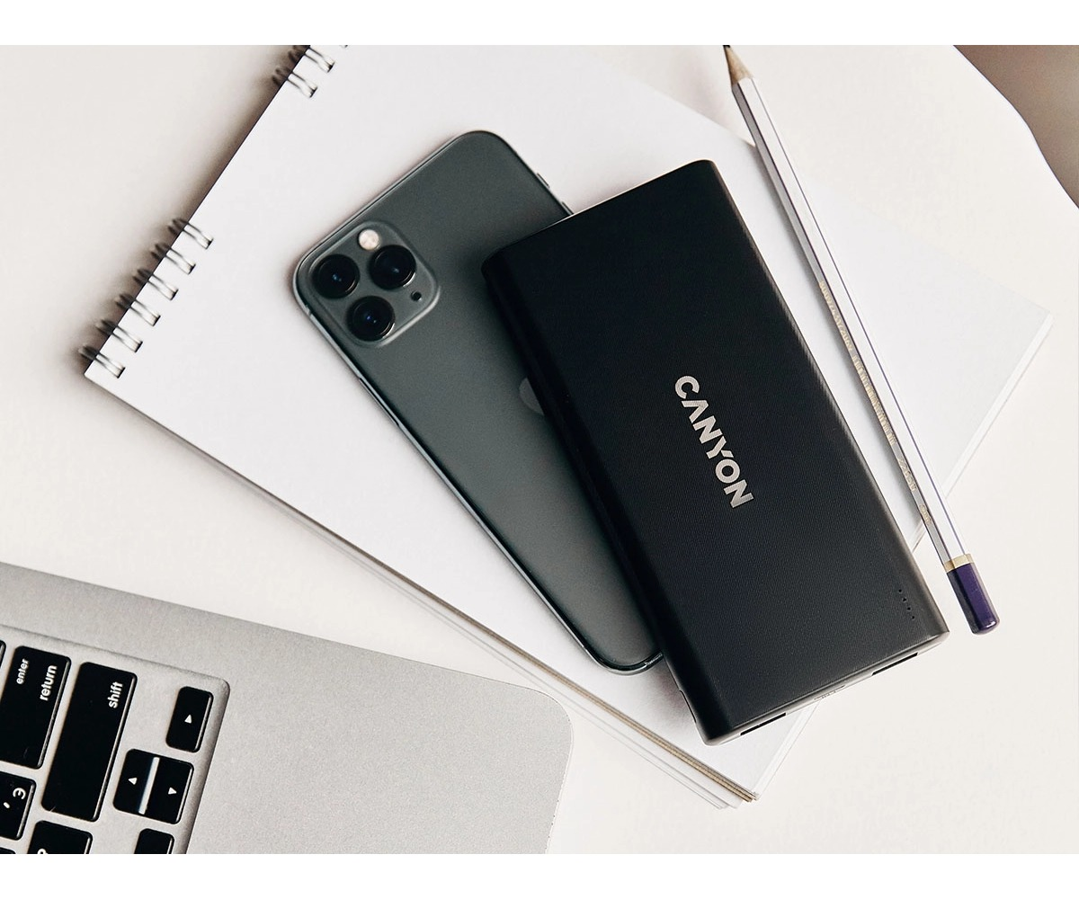 Smartfon, powerbank Canyon i ołówek na notesie obok laptopa.