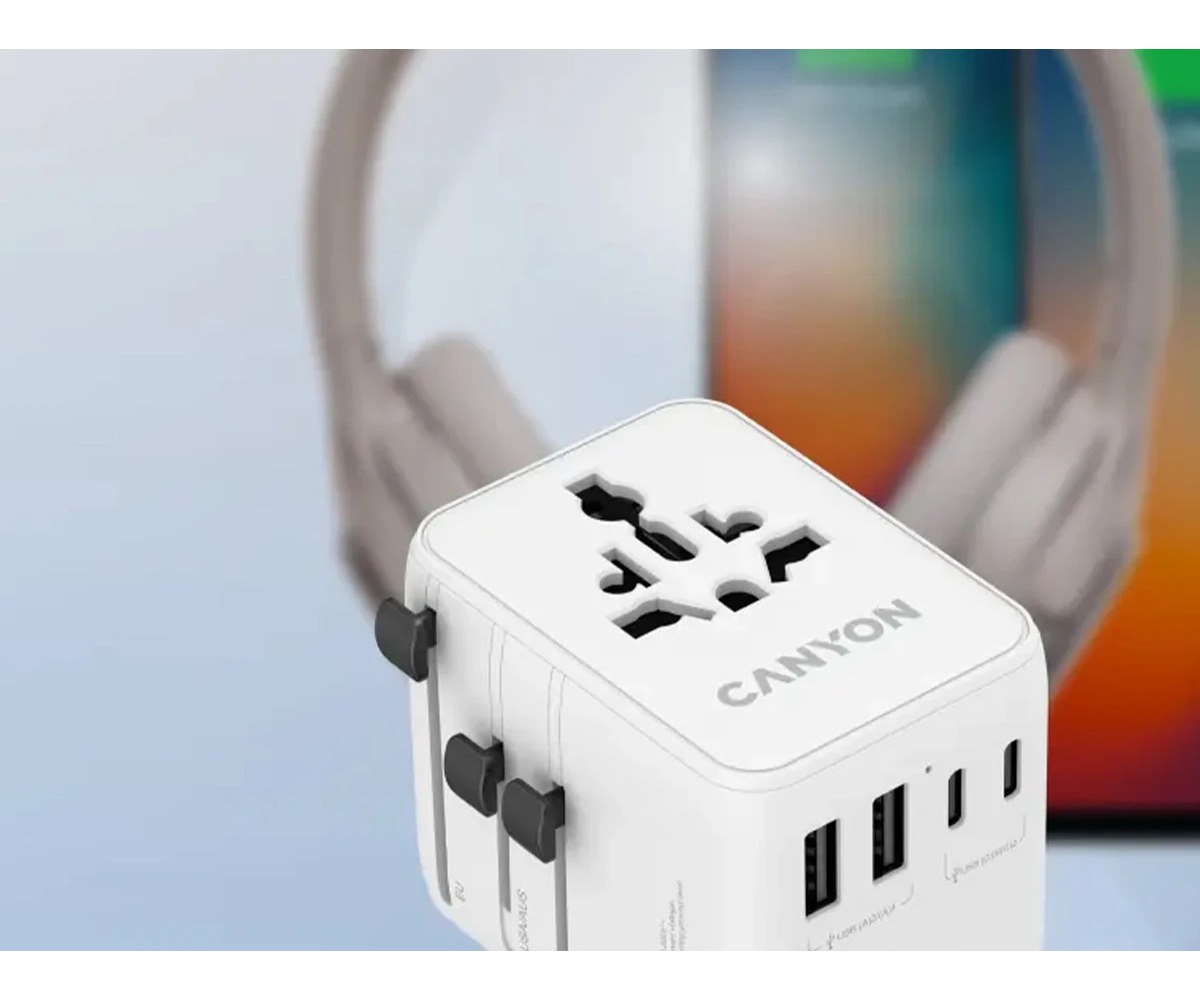 Biały adapter podróżny Canyon z portami USB na pierwszym planie, w tle słuchawki i tablet.