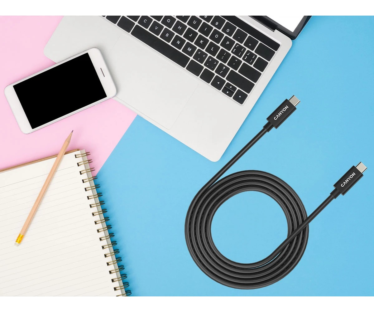 Zwinięty czarny kabel USB-C na niebiesko-różowym tle z laptopem, smartfonem i notesem.