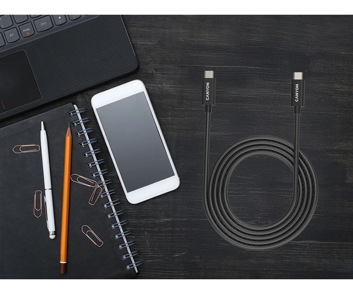 Czarny kabel USB Canyon leży obok laptopa, notatnika i smartfona na drewnianym biurku.