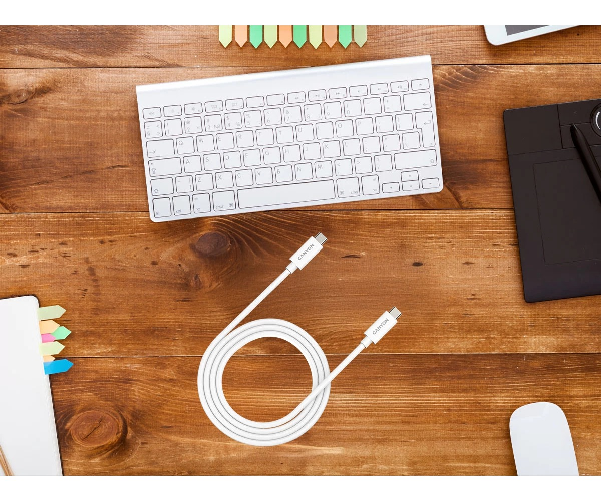 Zwinięty biały kabel USB-C na drewnianym biurku, w otoczeniu klawiatury, tabletu graficznego i notatnika.