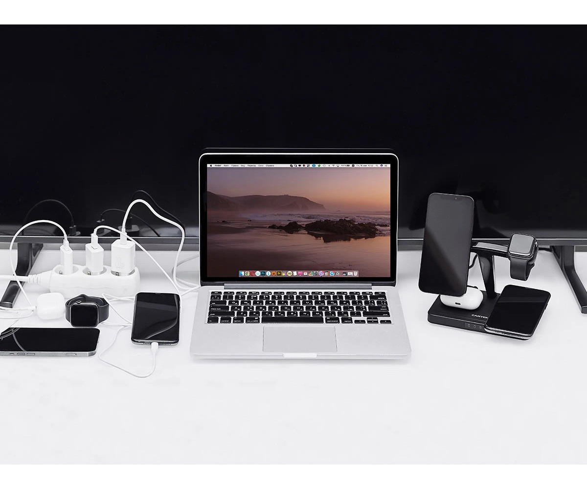 Laptop, stacja ładująca do wielu urządzeń, smartfony i listwa zasilająca na białym biurku.