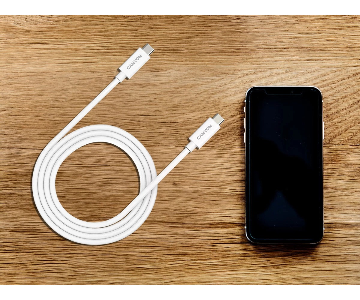 Biały kabel USB-C Canyon i smartfon leżą obok siebie na drewnianej powierzchni.