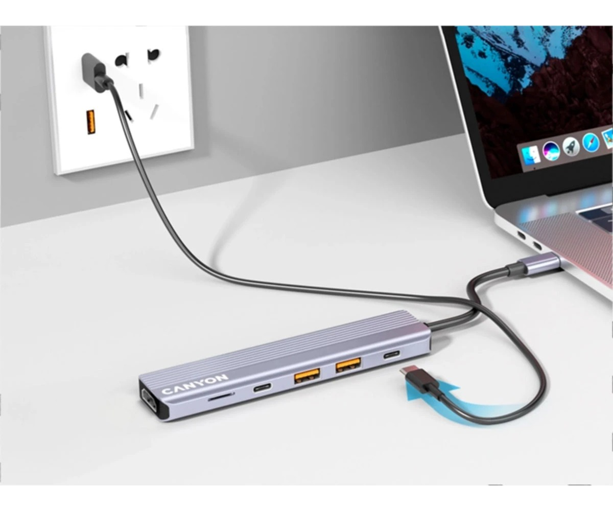 Hub USB-C Canyon podłączony do laptopa i gniazdka ściennego na białym biurku.