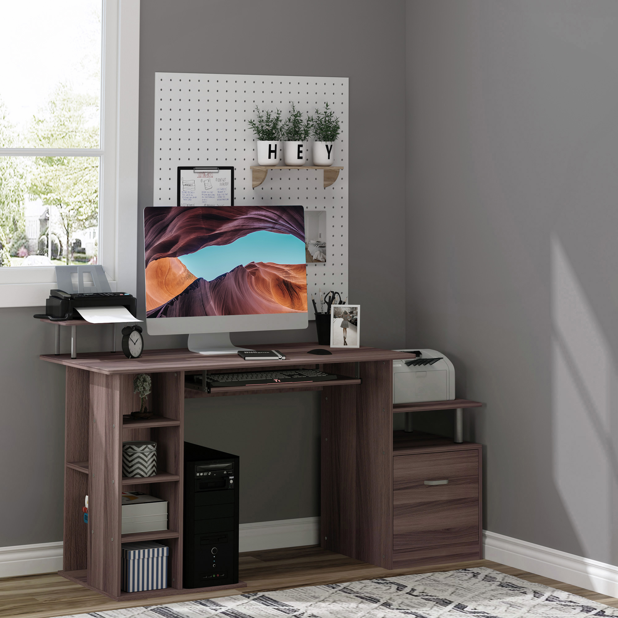 Una scrivania in legno ordinata con computer, stampante, mensole e pannello forato con piante nell'angolo di una stanza.