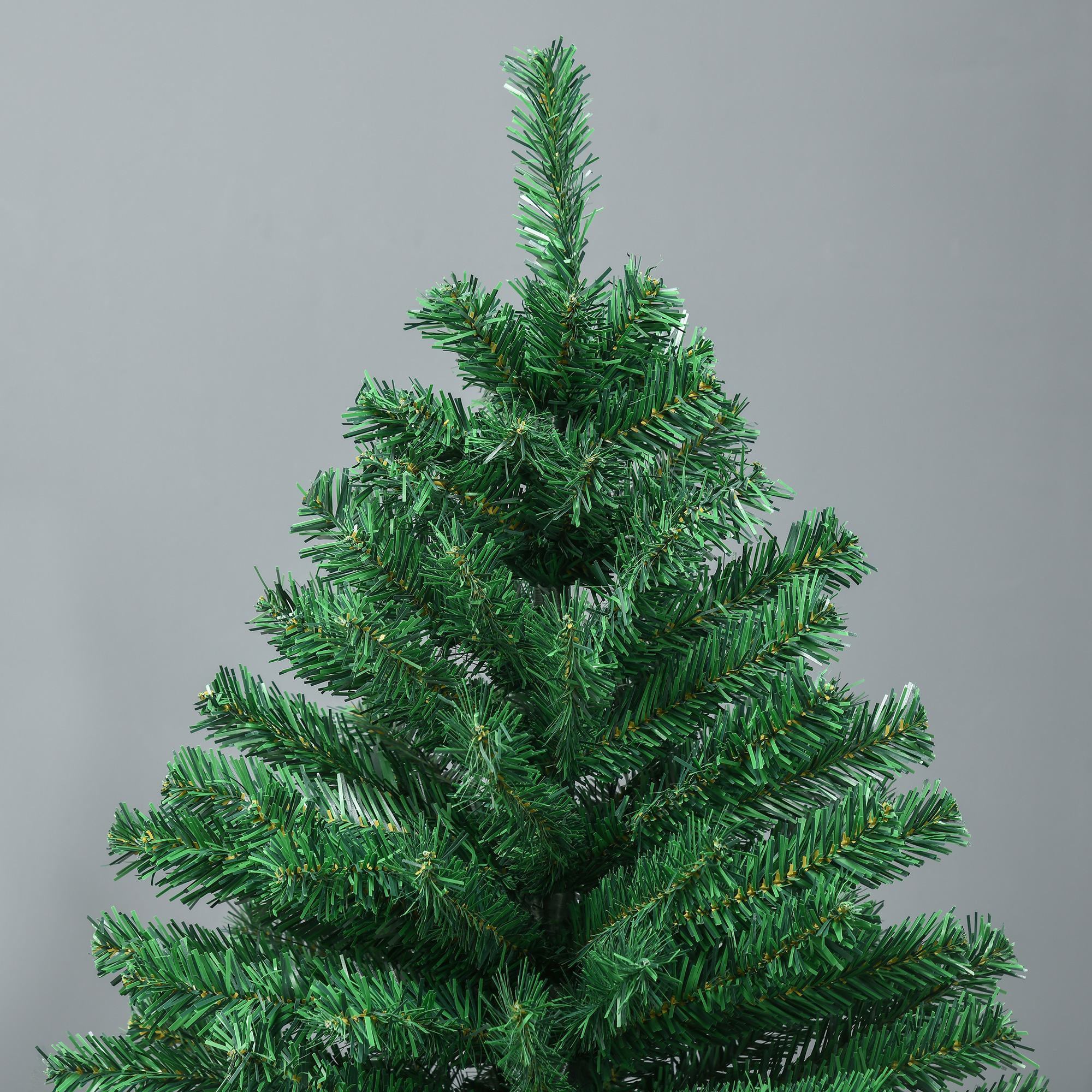Primer plano de la parte superior verde de un árbol de Navidad artificial sobre un fondo gris liso.