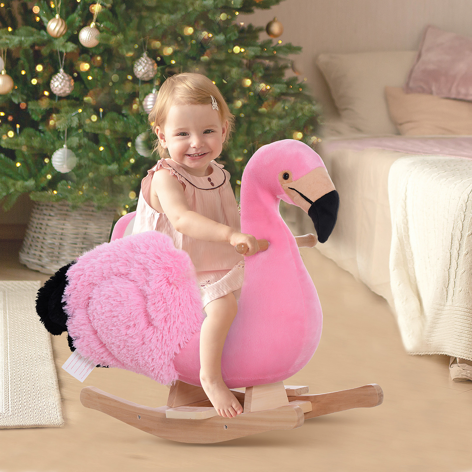 Bambina sorridente seduta su un giocattolo a dondolo a forma di fenicottero rosa davanti a un albero di Natale.