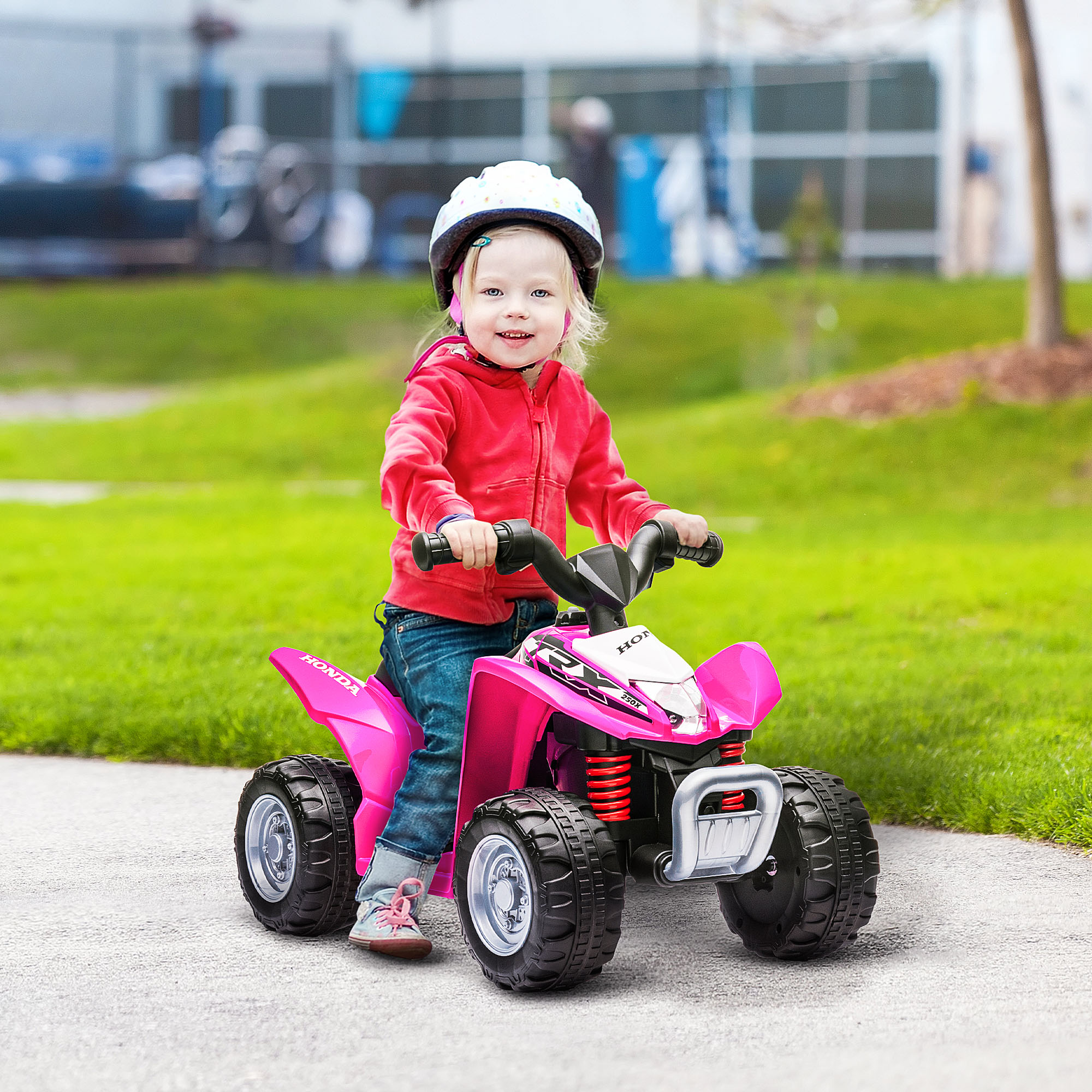 Una bambina con casco guida un quad giocattolo rosa all'aperto su un sentiero asfaltato.