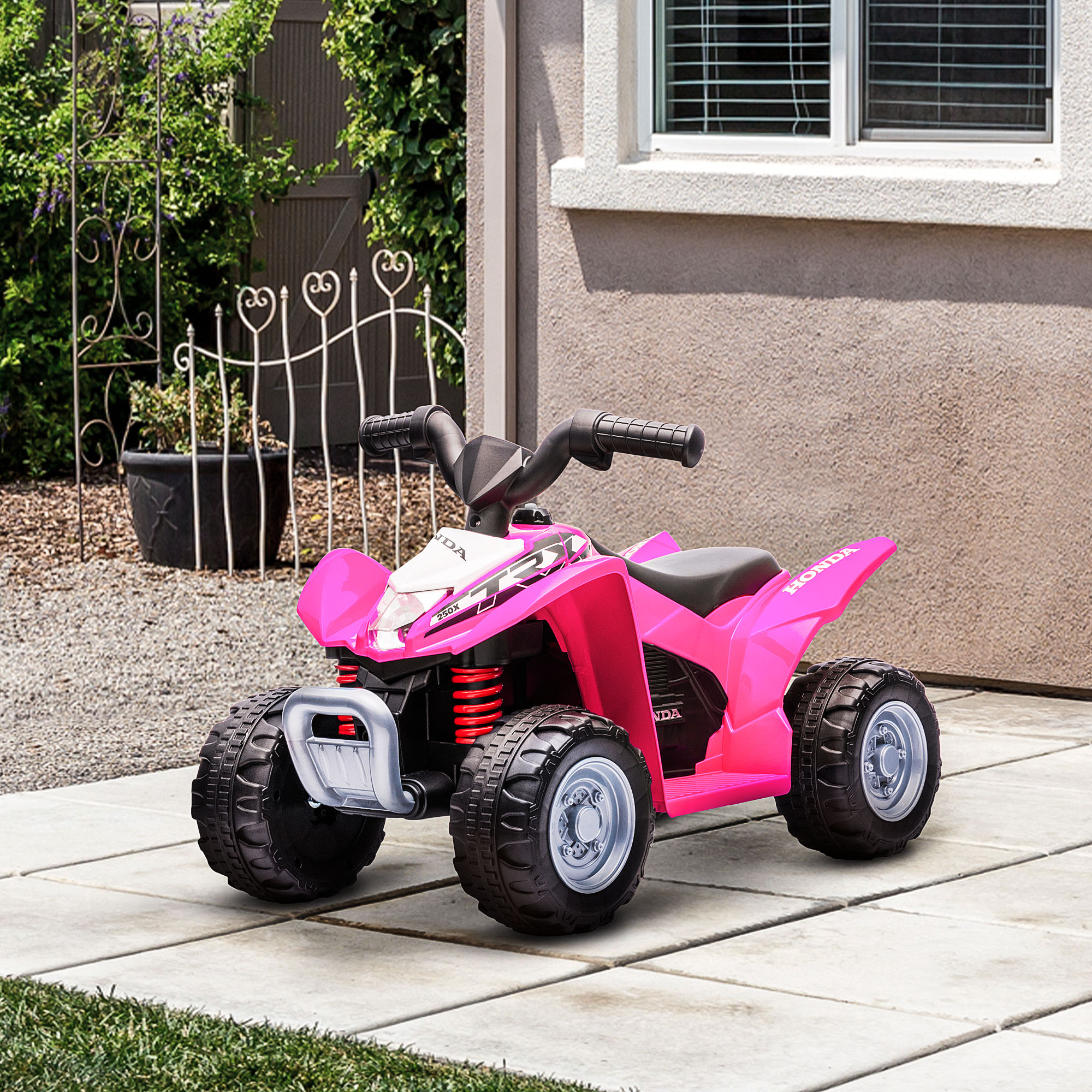 Un quad per bambini rosa con grandi ruote nere si trova su un patio davanti al muro di una casa.