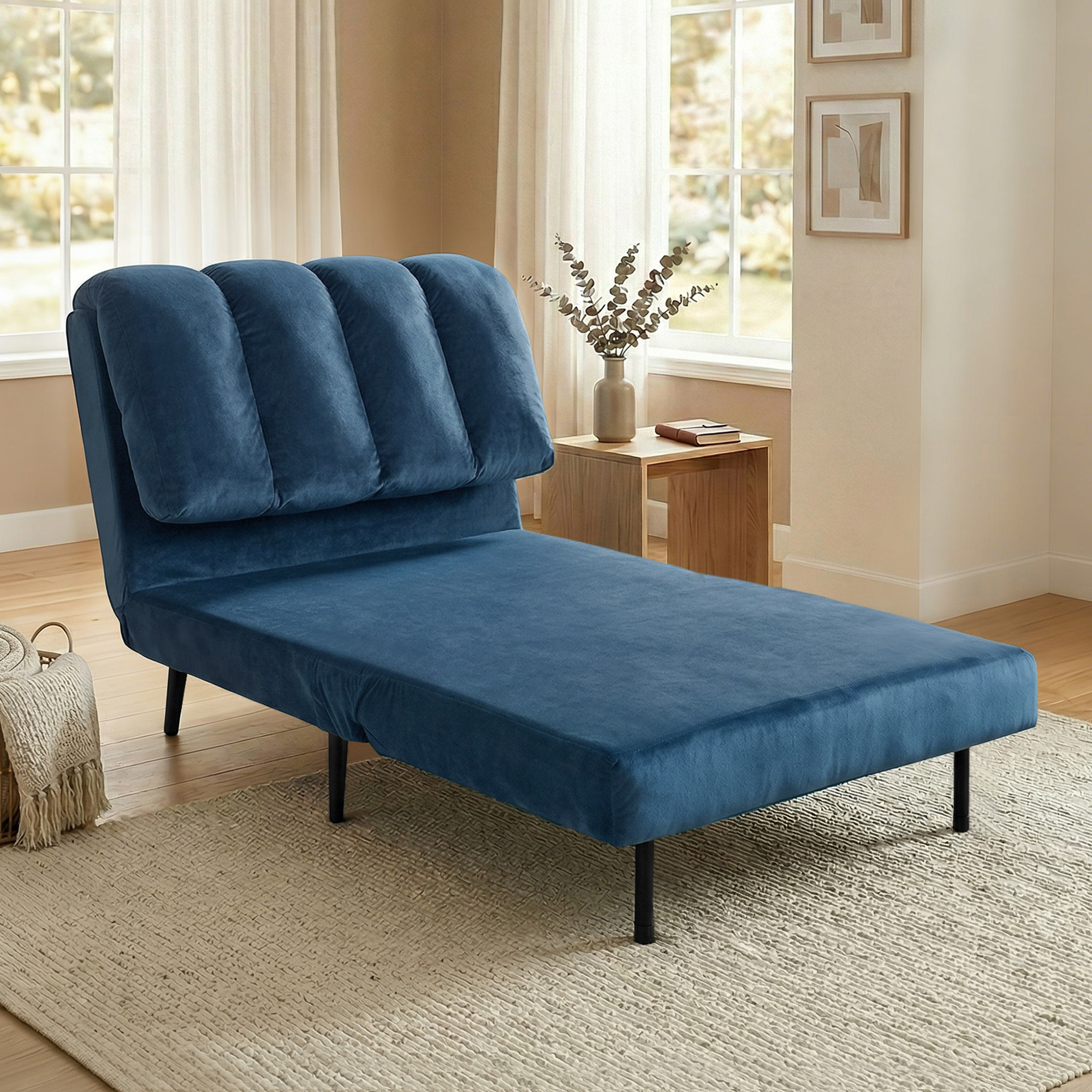 Una chaise longue in velluto blu si trova su un tappeto chiaro in una stanza luminosa con un piccolo tavolino.