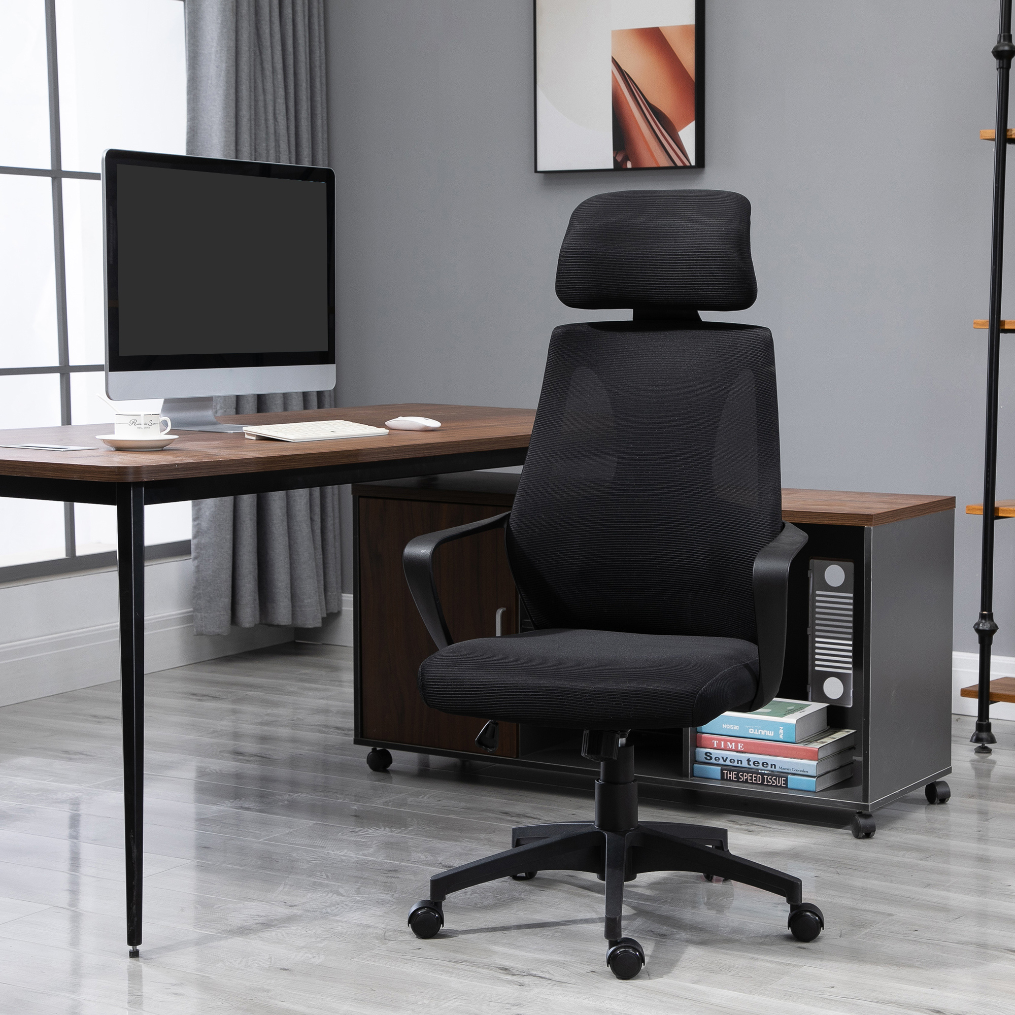 Una sedia da ufficio ergonomica nera davanti a una scrivania con computer in un ufficio moderno.