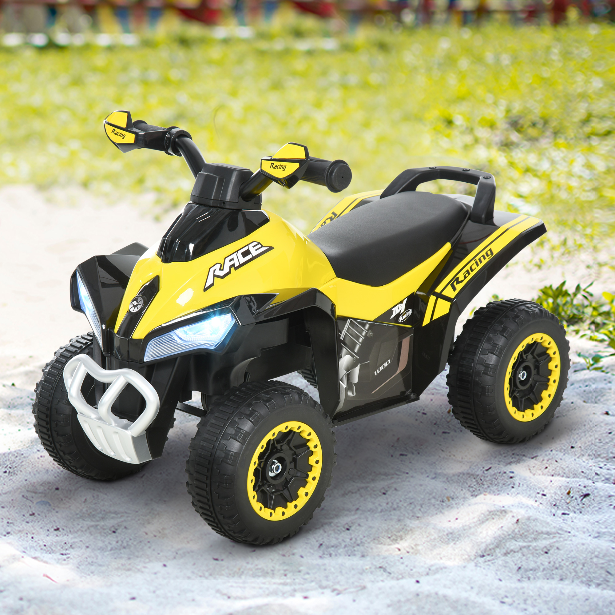 Un quad per bambini giallo e nero con fari su sabbia chiara davanti a un prato verde.