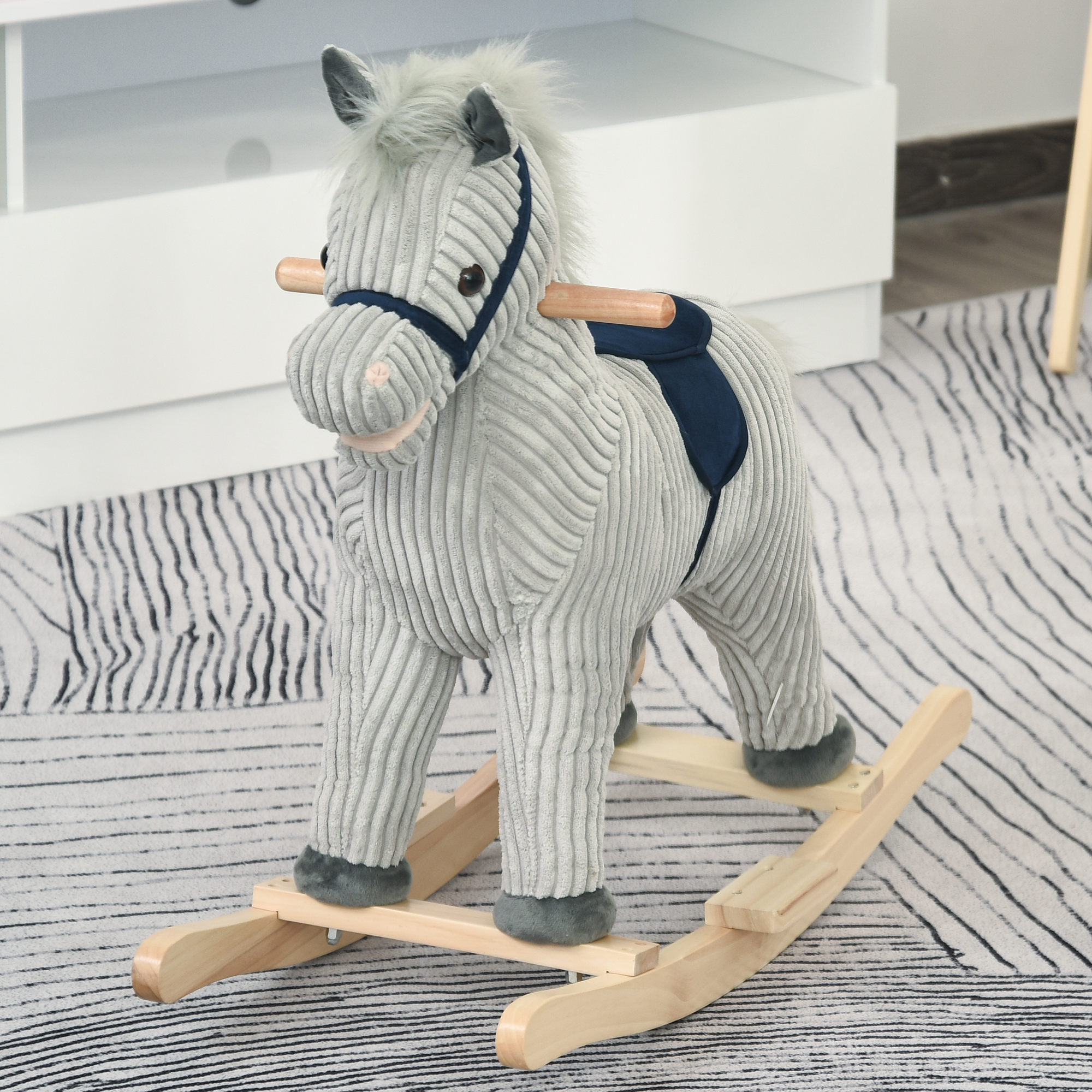 Un cavallo a dondolo di peluche grigio con basi in legno e sella scura su un tappeto.