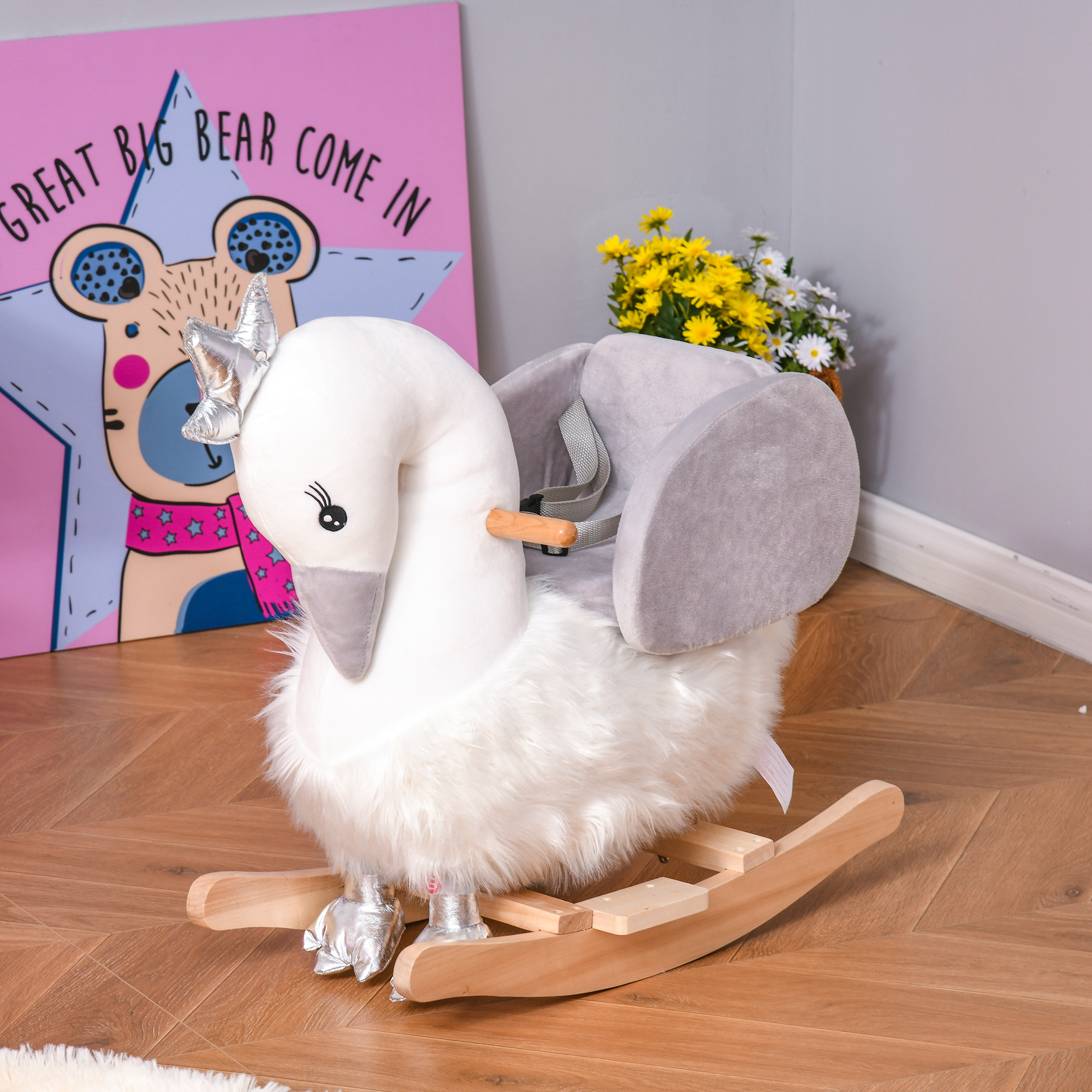 Un cigno a dondolo di peluche bianco con ali grigie e dondoli in legno, davanti a un quadro colorato.