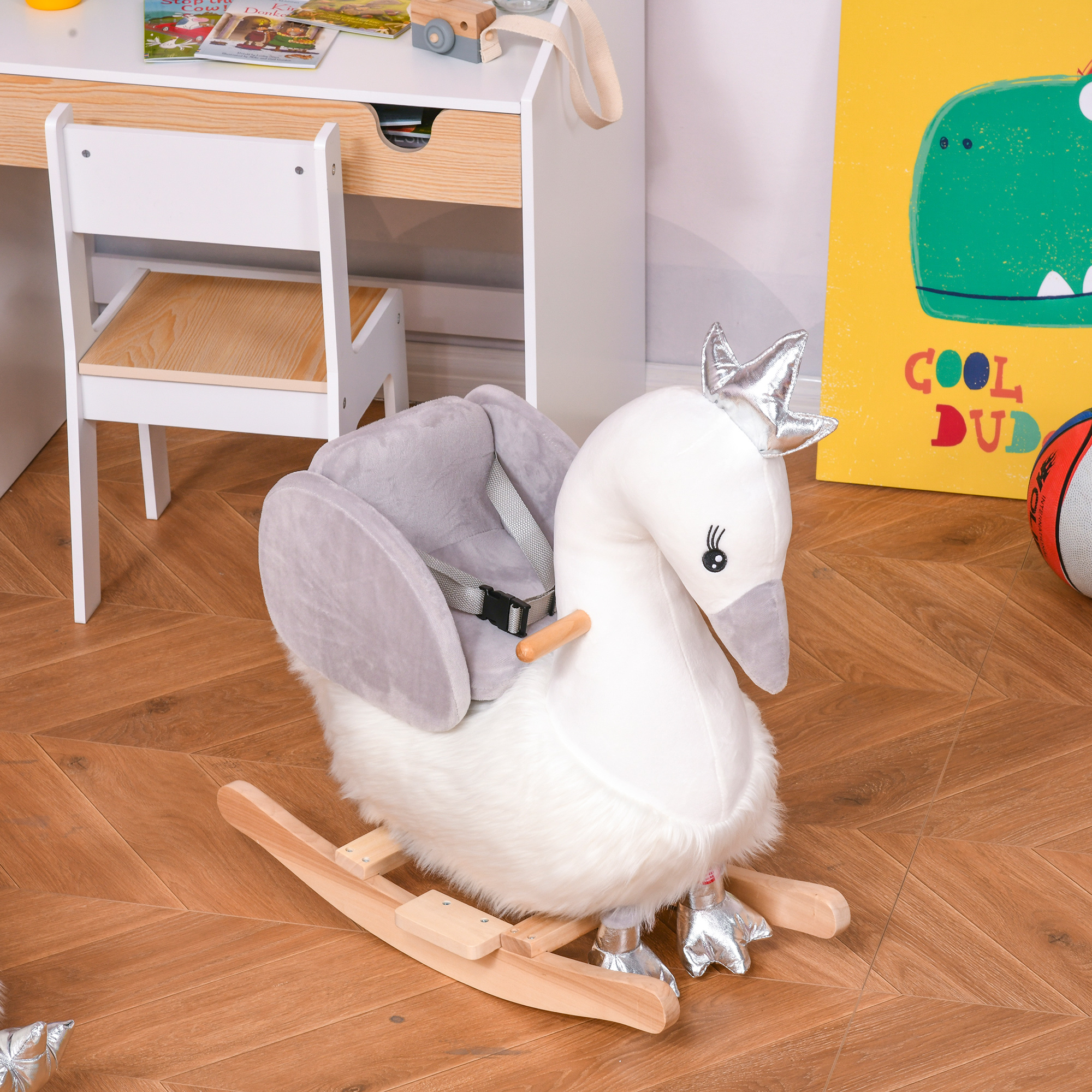 Un dondolo a forma di cigno bianco in peluche con corona argentata e ali grigie su base di legno in una stanza.