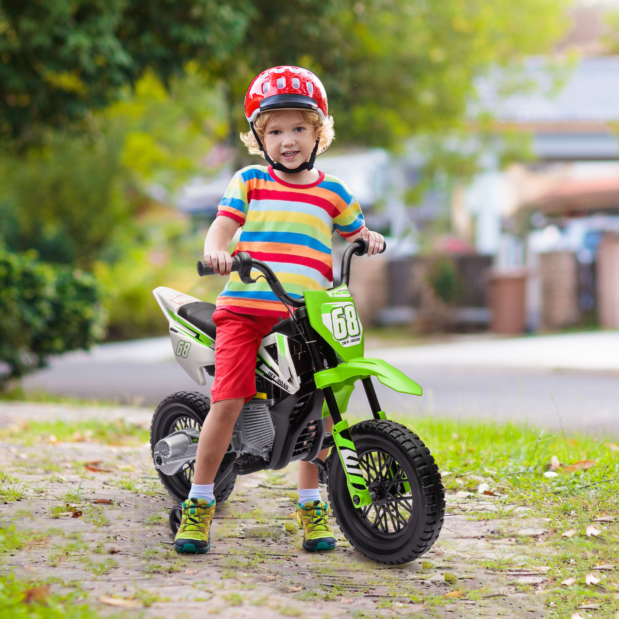 Un bambino con casco rosso siede su una moto giocattolo verde all'aperto.