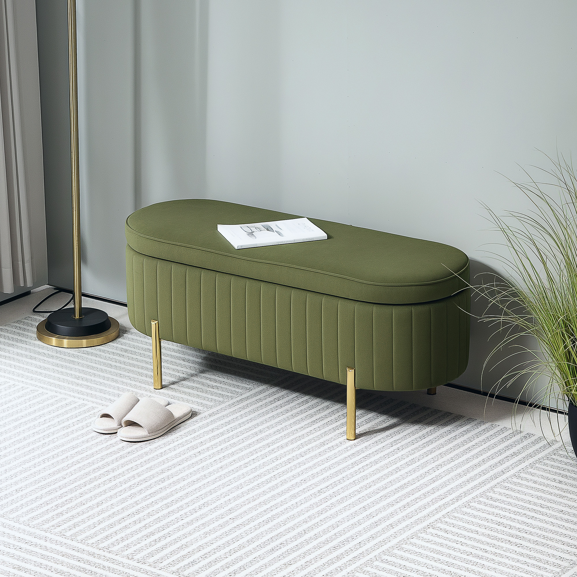 Una panca imbottita verde con gambe dorate su un tappeto, con pantofole e una pianta.