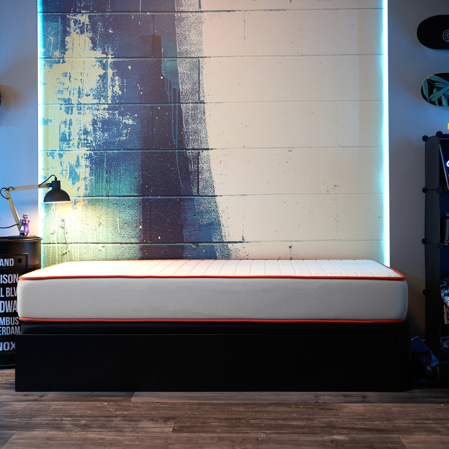 Una cama con un colchón blanco y borde naranja contra una pared de ladrillo pintada con luz de neón azul.