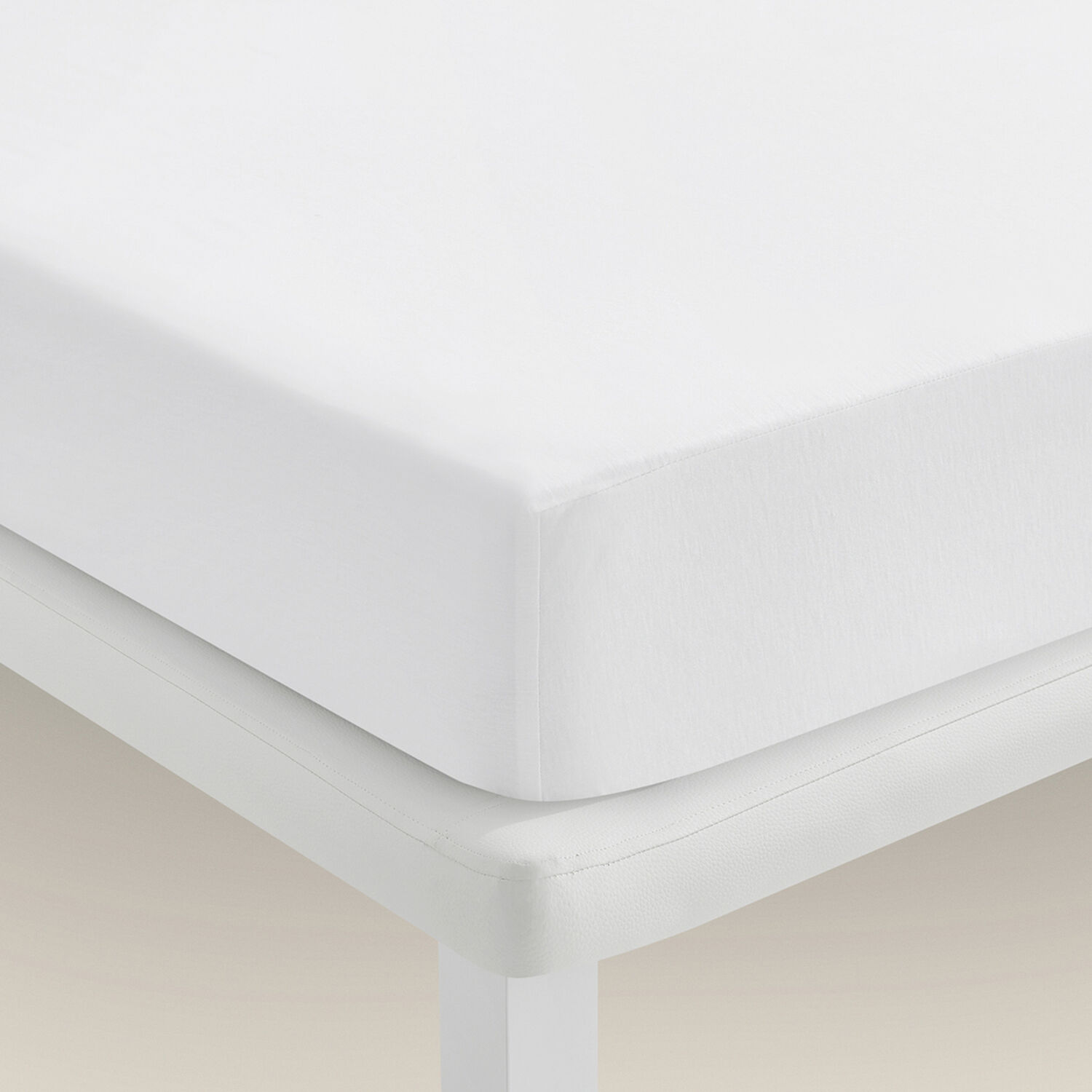 Una cama blanca con una sábana bajera blanca sobre fondo blanco.