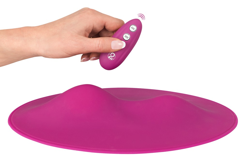 Eine Hand hält eine pinke Fernbedienung über ein pinkes Pad mit zwei Hügeln.