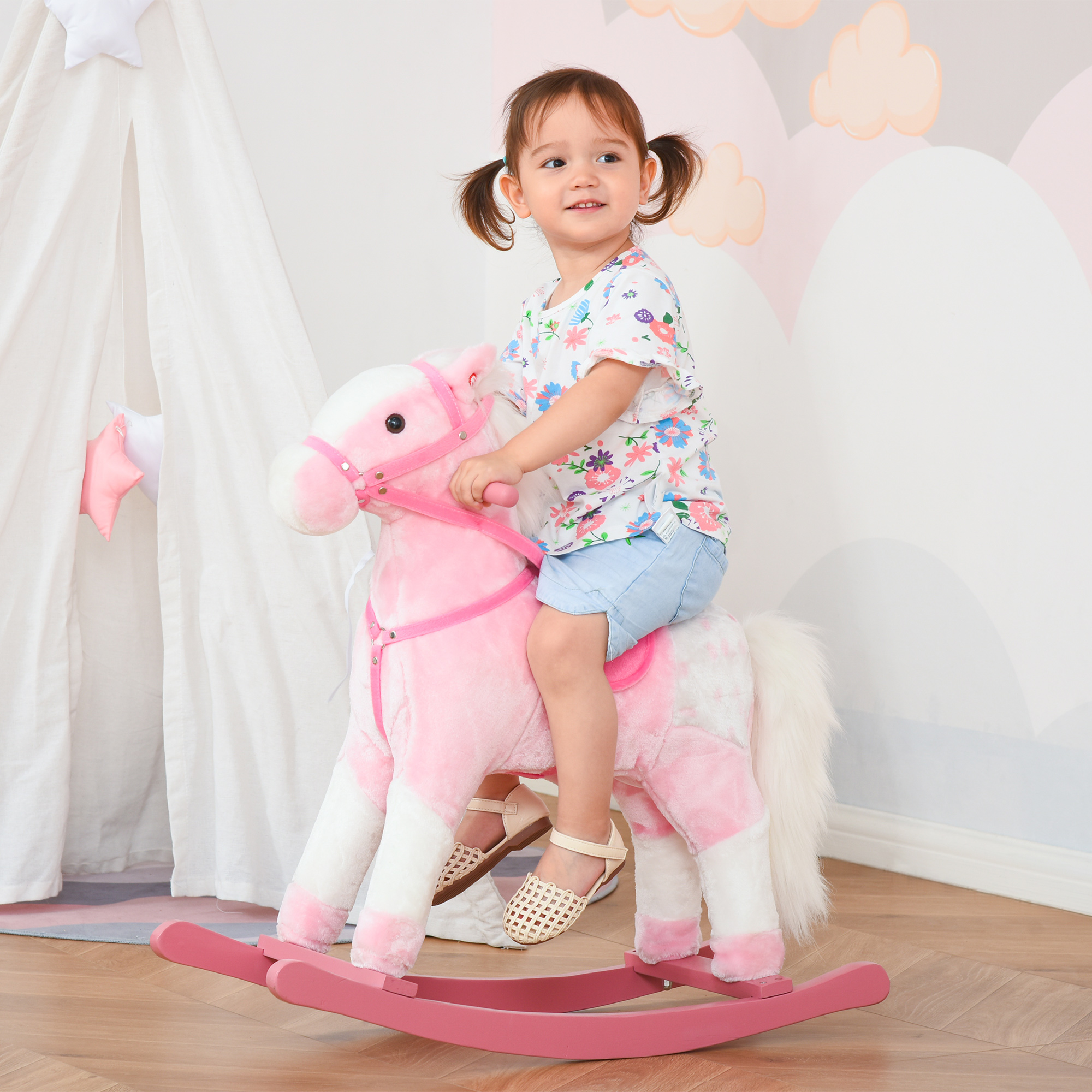 Una bambina cavalca un cavallo a dondolo di peluche rosa in una stanza luminosa con una tenda da gioco.