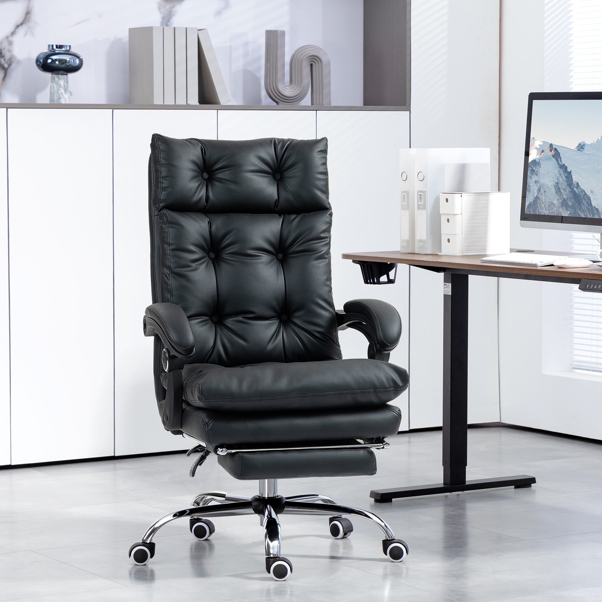 Una sedia da ufficio in pelle nera con rotelle di fronte a una scrivania con computer.