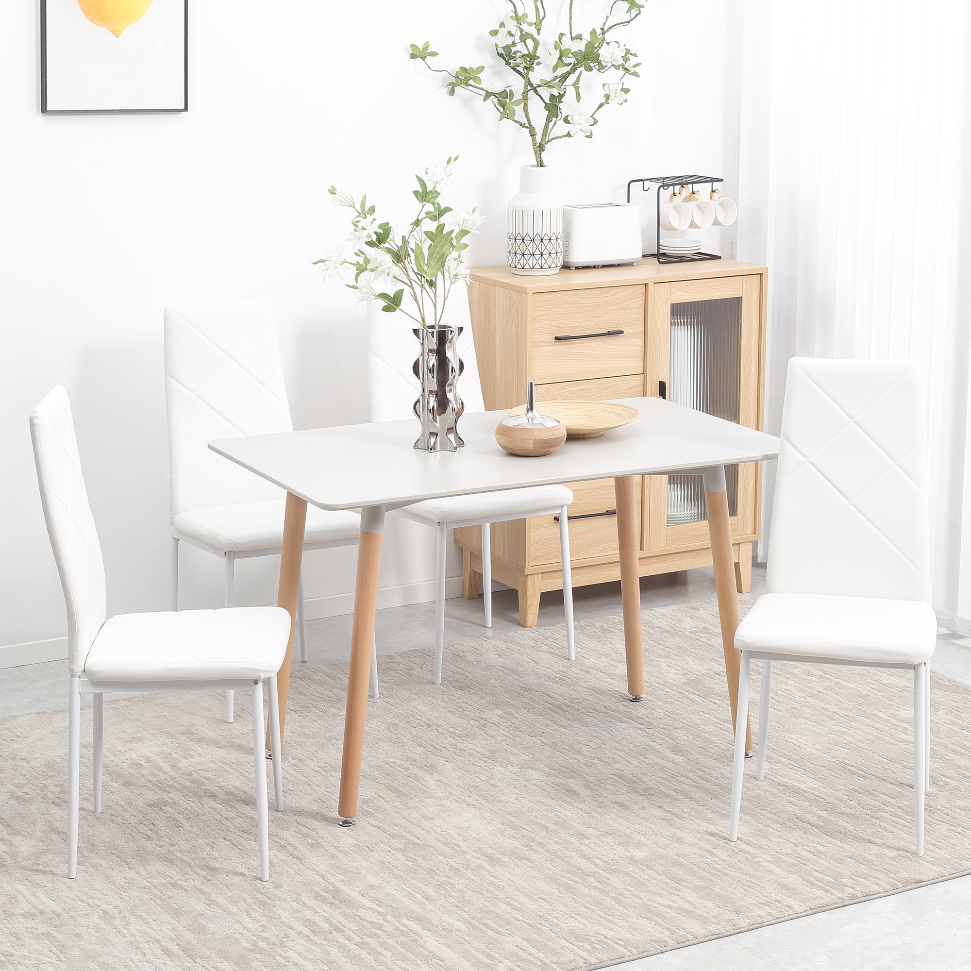Un tavolo da pranzo bianco con quattro sedie bianche si trova su un tappeto grigio in una stanza luminosa con mobili in legno.