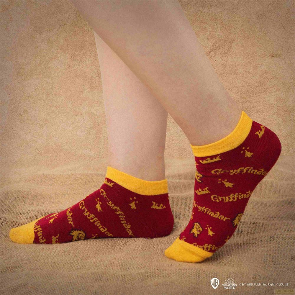 Persona con calcetines de Gryffindor rojo oscuro y amarillo sobre fondo arenoso.