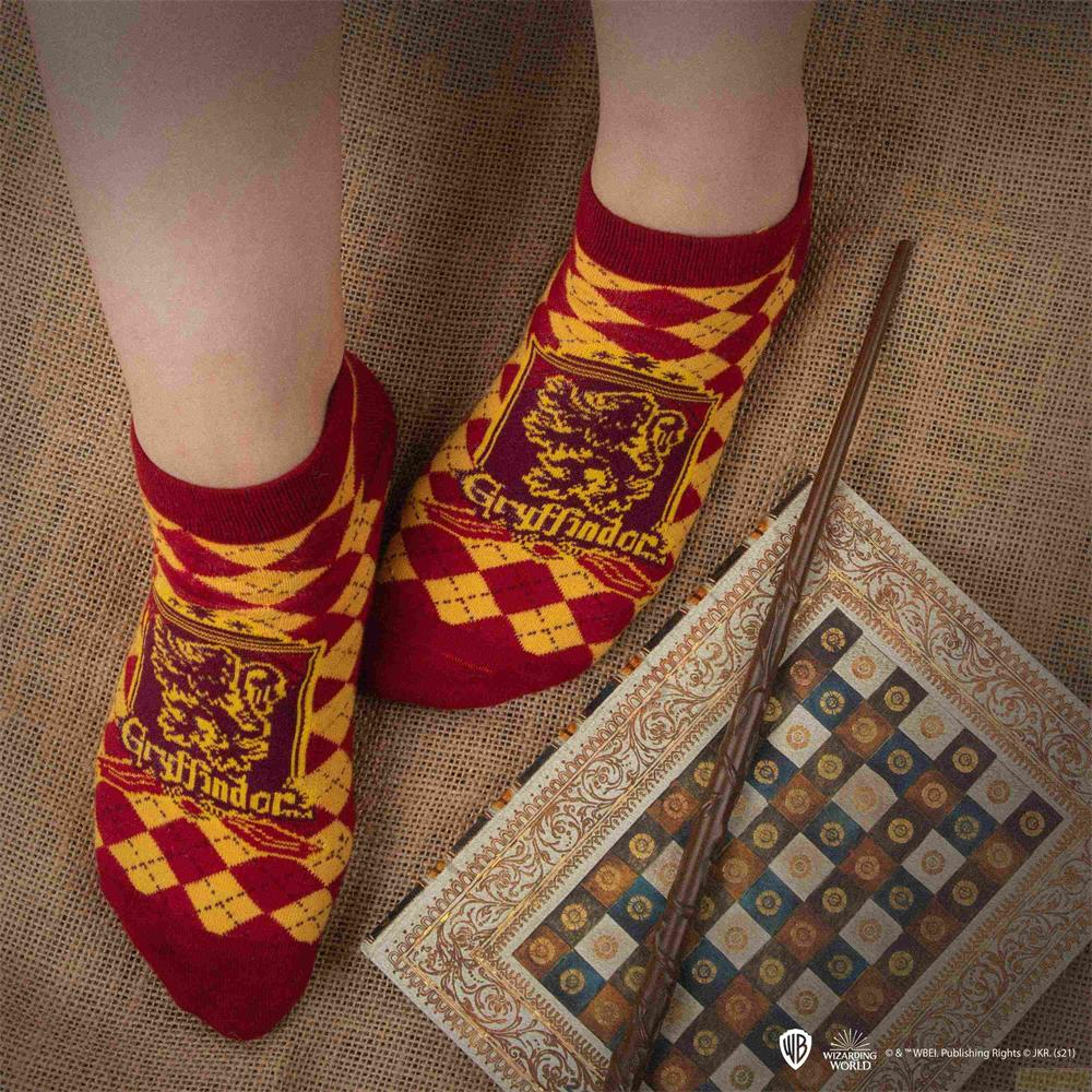 Persona usa calcetines de Gryffindor rojos y dorados junto a un libro adornado y una varita sobre yute.