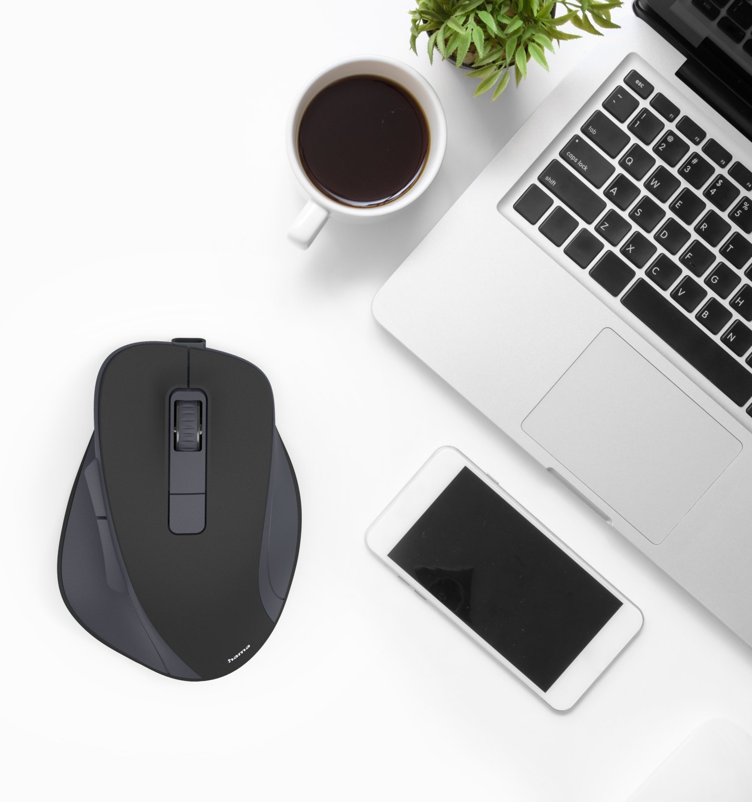 Vista superior de un escritorio blanco con un portátil, un ratón, un smartphone, una taza de café y una planta en maceta.