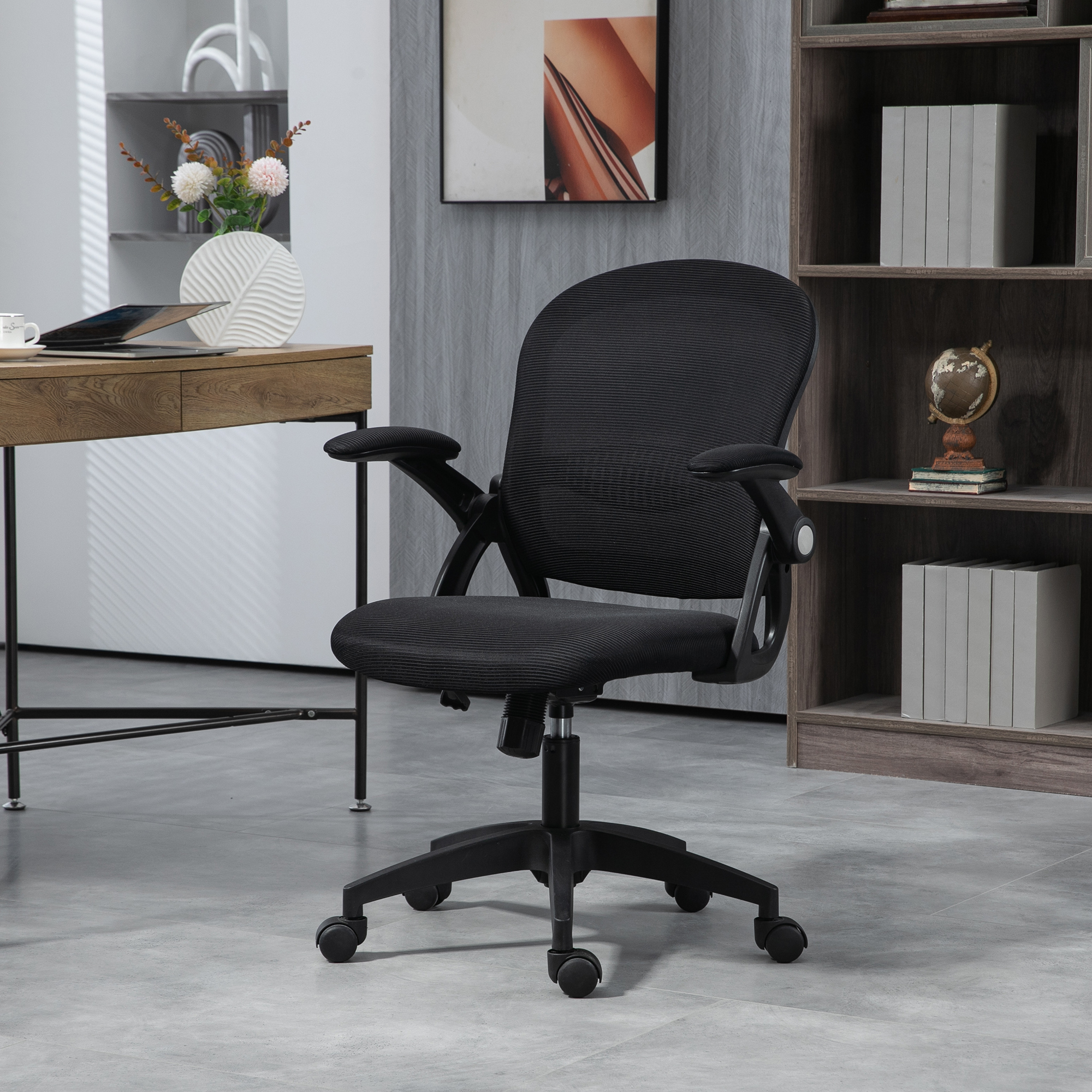 Una sedia da ufficio in rete nera su pavimento grigio in una stanza moderna con scrivania in legno e libreria.