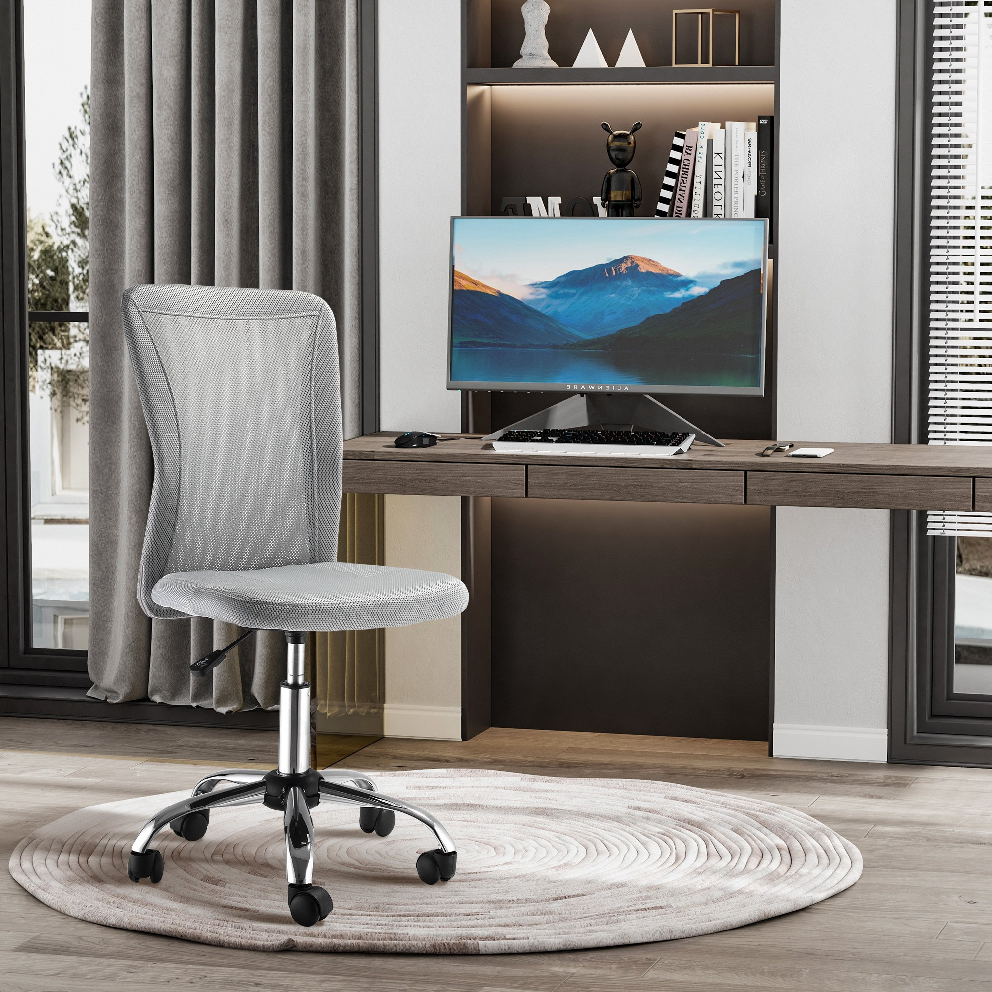 Una sedia da ufficio in rete grigia su un tappeto rotondo davanti a una scrivania in legno con computer.