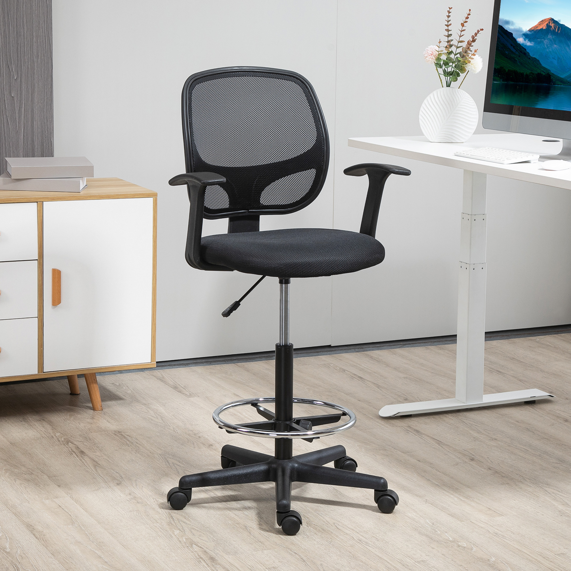 Una sedia da disegno in rete nera si trova su un pavimento in legno chiaro in un ufficio moderno, accanto a una scrivania.