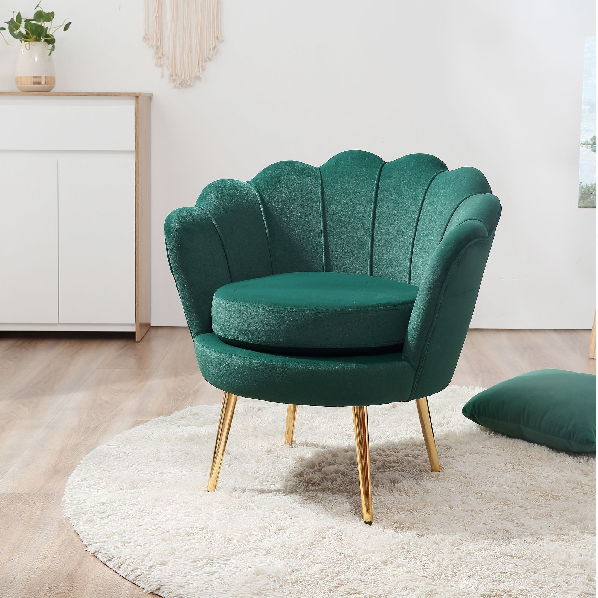 Una poltrona in velluto verde scuro con design a conchiglia e gambe dorate si trova su un tappeto bianco rotondo.