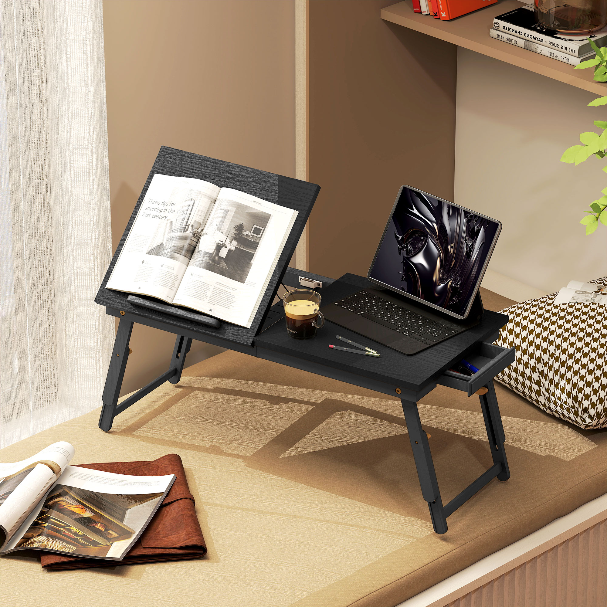 Una mesa de cama para portátil negra sostiene un libro abierto, una tableta, café y bolígrafos.