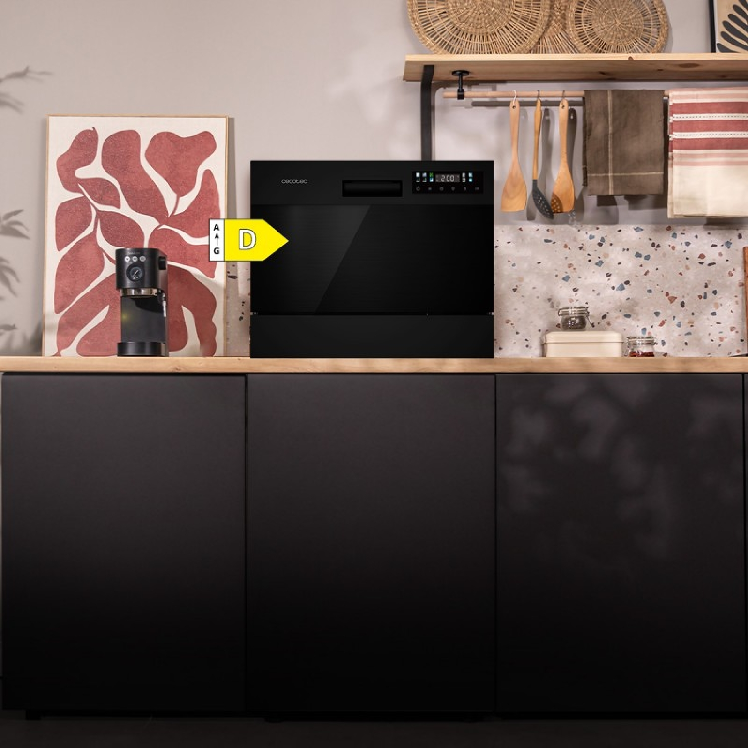 Lavavajillas negro sobre encimera de madera en una cocina moderna con cafetera y arte.