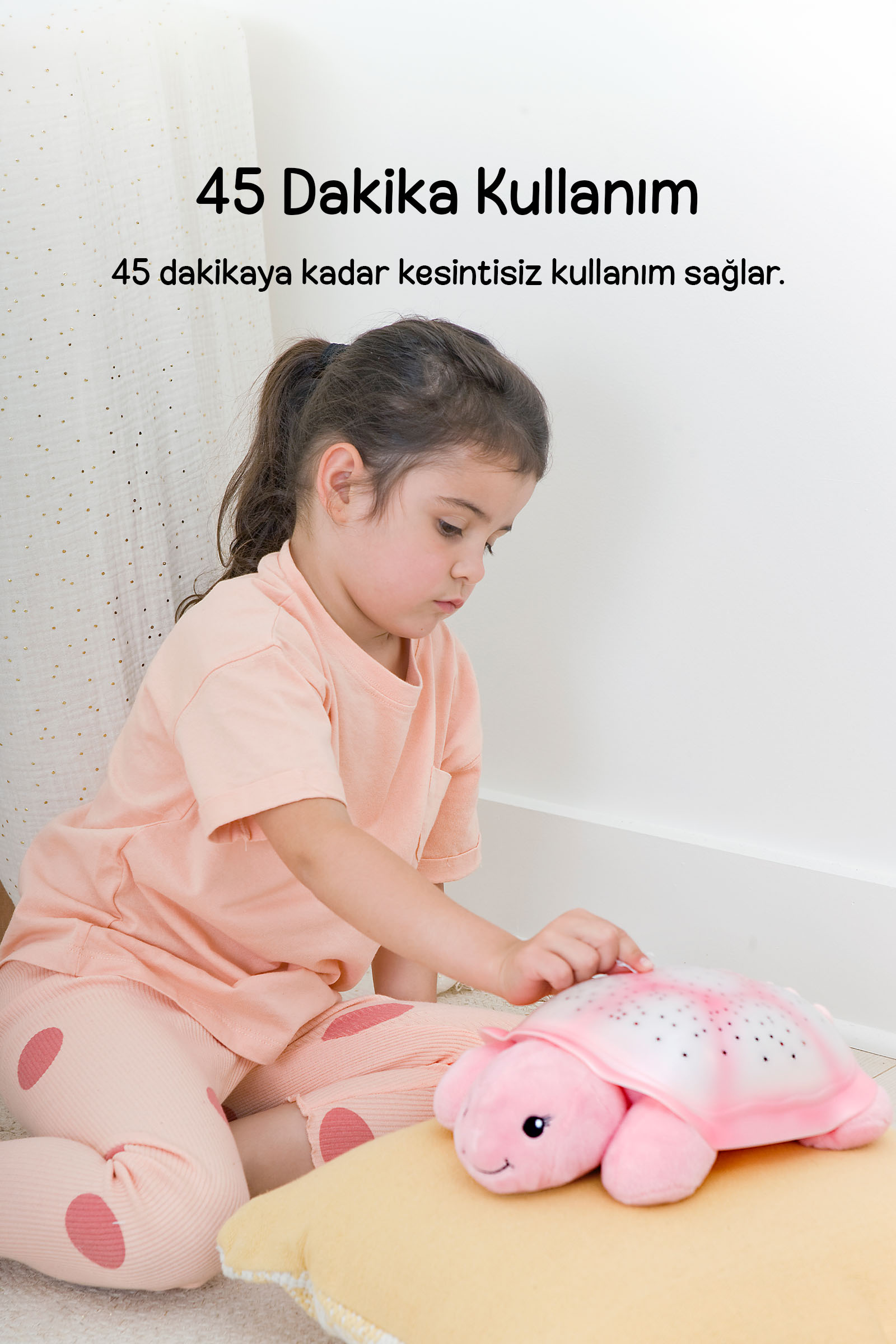 Pembe pijamalı küçük kız, sarı minder üzerindeki pembe kaplumbağa gece lambasını açıyor.