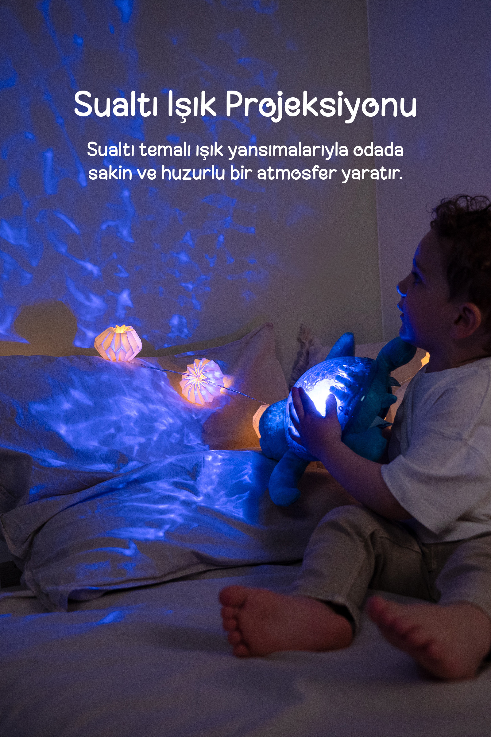 Bir çocuk yatakta parlayan peluş bir kaplumbağa tutarken duvara mavi ışık desenleri yansıtılıyor.