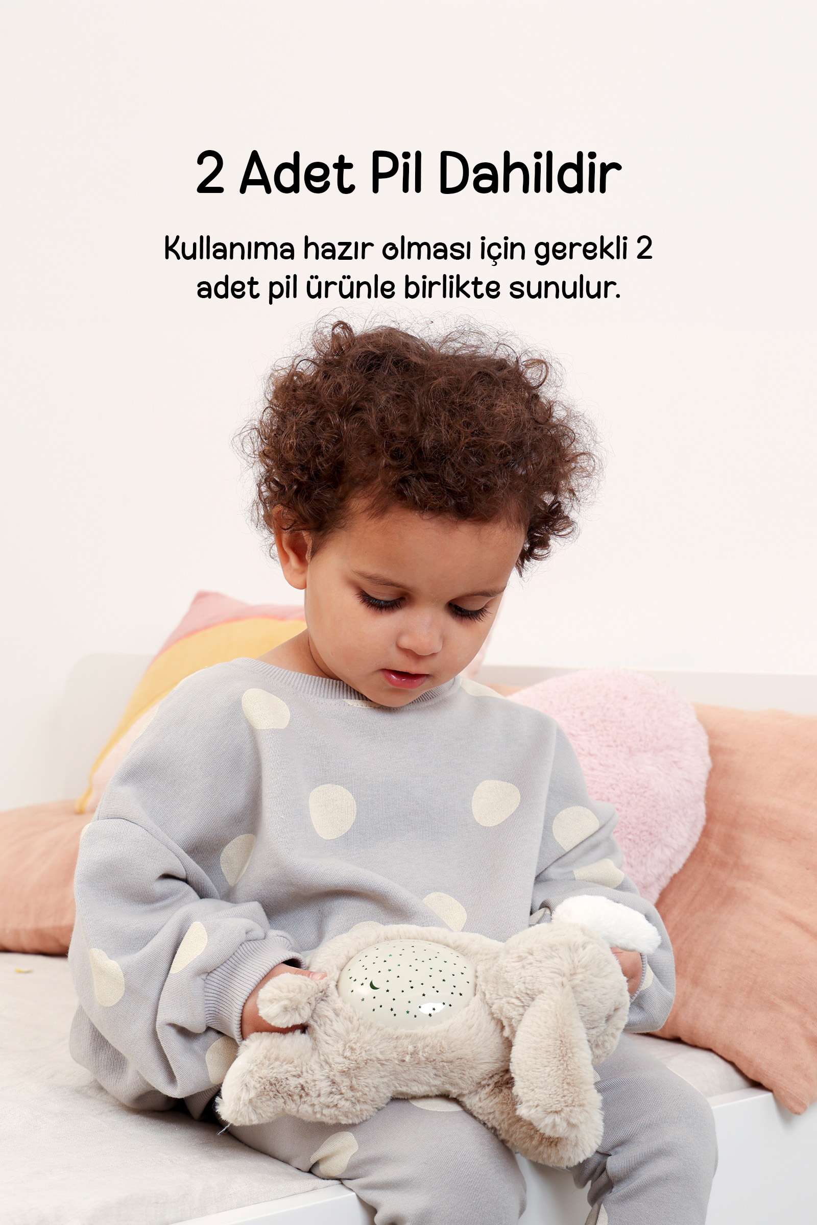 Kivircik sacli bir cocuk pastel renkli yastiklarin onunde pelus tavsan tutuyor.