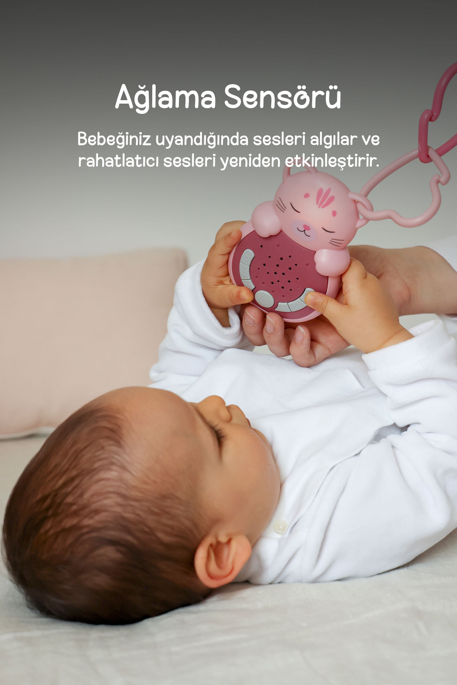 Yatan bir bebek, arka planda yastık ve Türkçe metin ile pembe kedi oyuncak tutuyor.