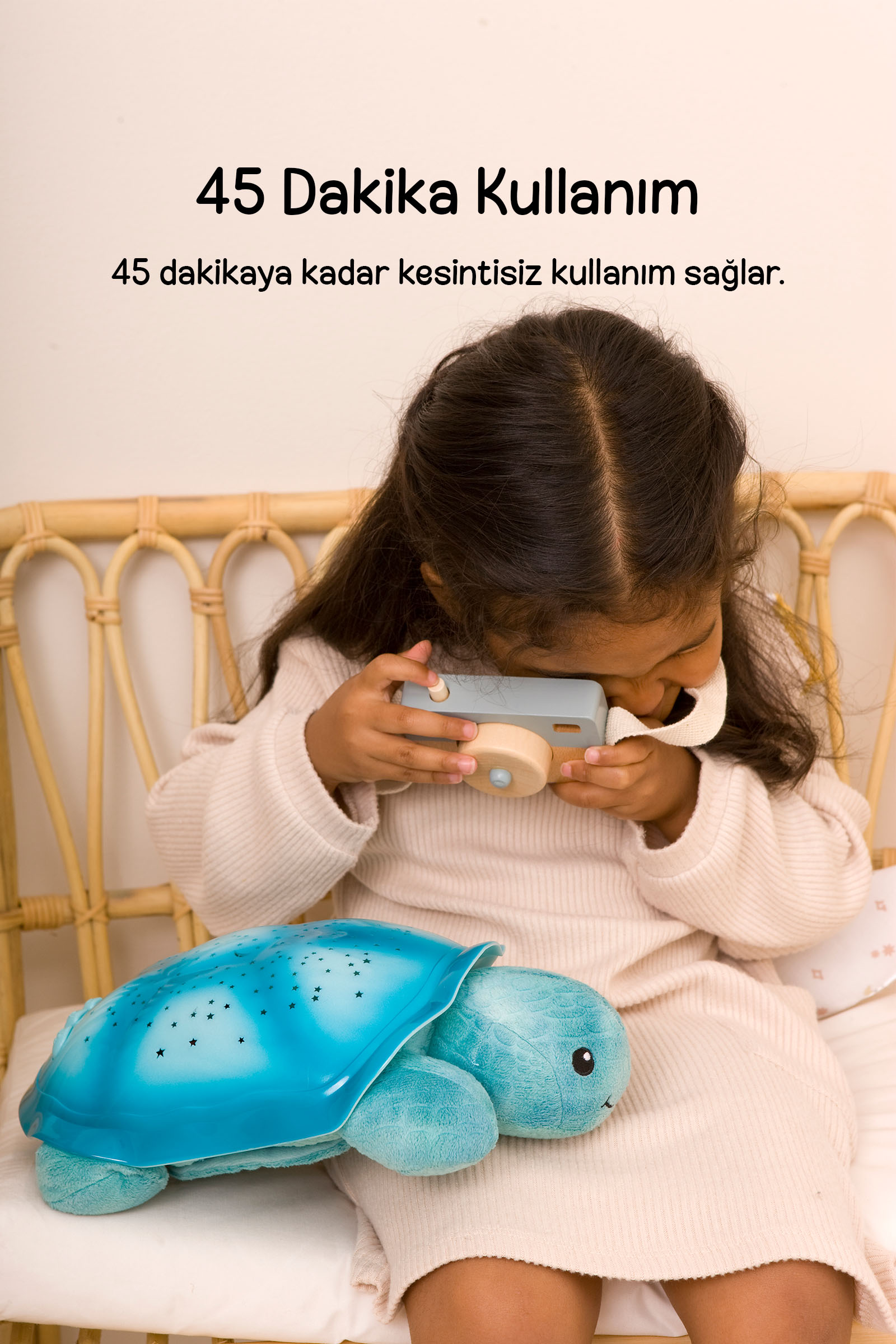 Genç bir kız, rattan bir sandalyede mavi kaplumbağa gece lambasının yanında oyuncak kamera tutuyor.