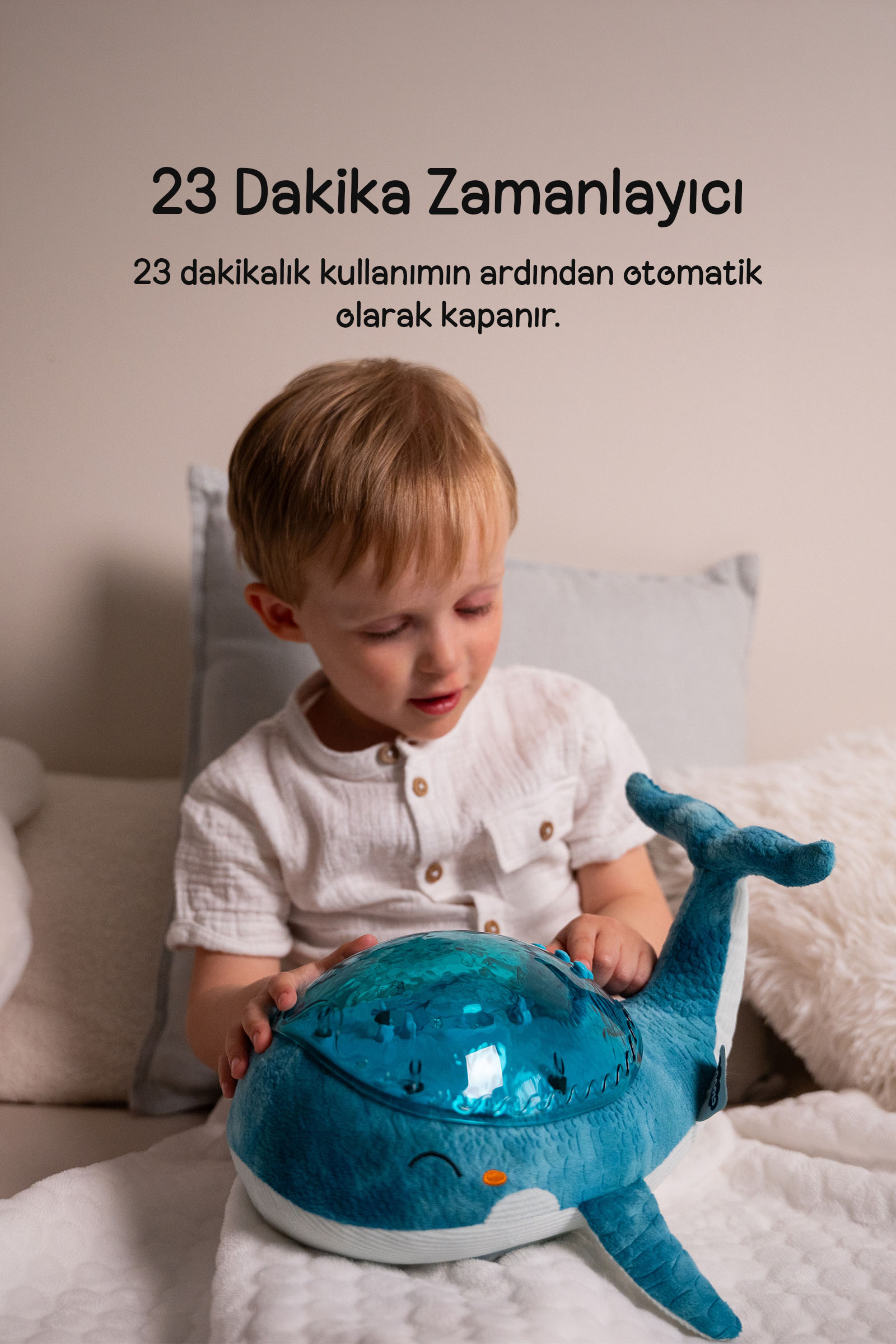 Yatakta oturan küçük çocuk, mavi balina gece lambasıyla oynuyor.