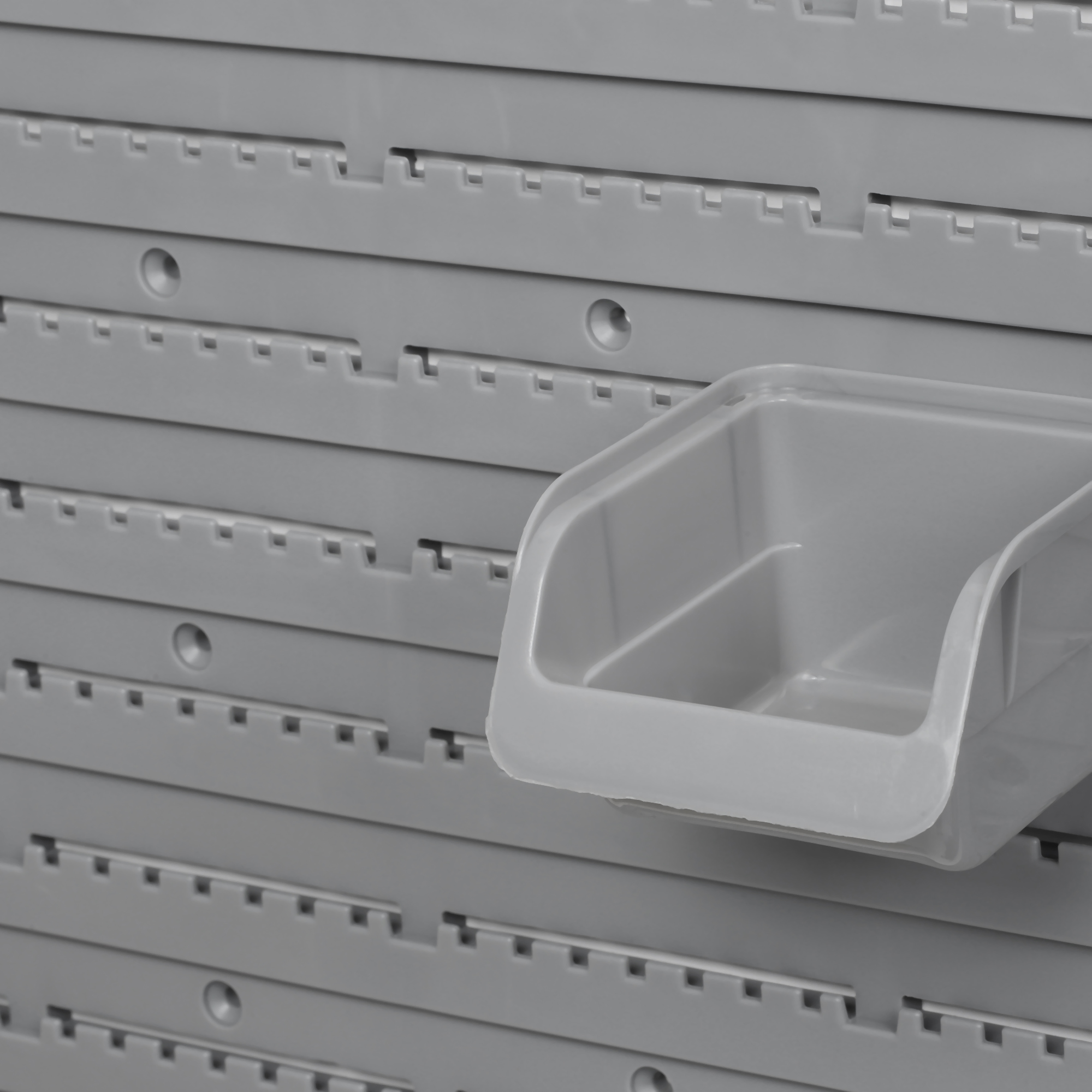 Una sola caja de almacenamiento gris está fija en un panel de pared ranurado de plástico gris.