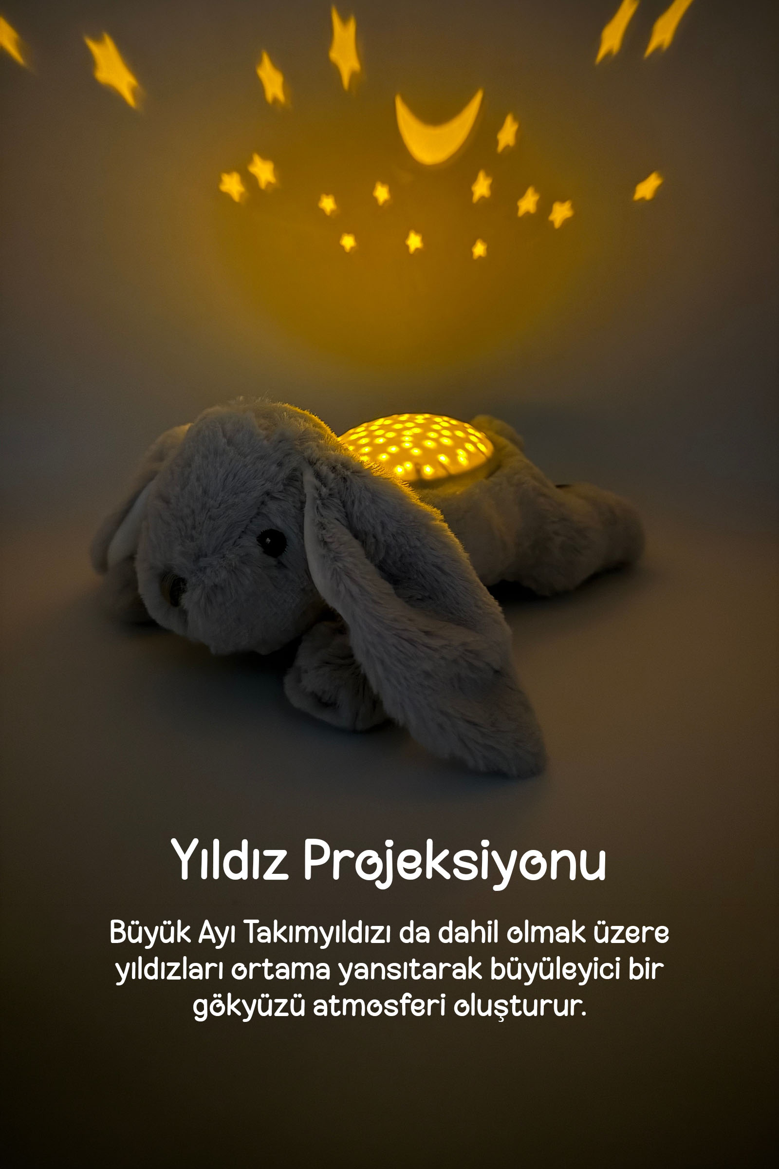 Gri renkli peluş oyuncak duvara sarı yıldızlar ve aylar yansıtıyor.